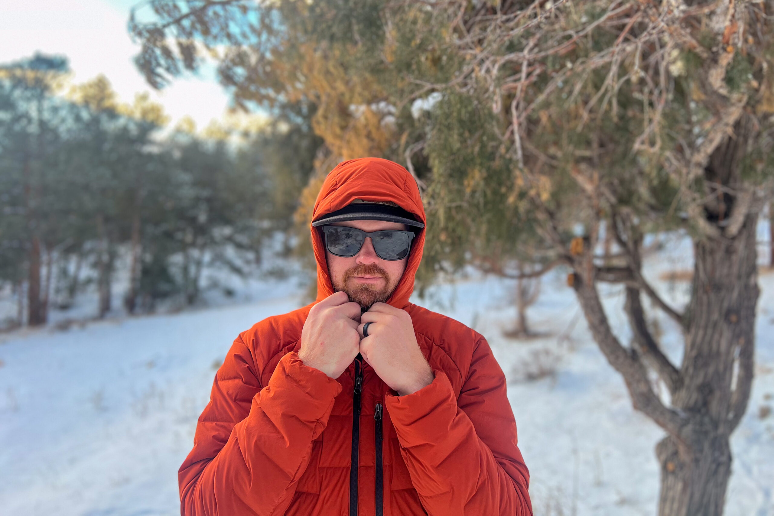 A person tightening the hood of the Mountain Hardwear StretchDown Hoody while wearing sunglasses, standing in a snowy forest setting.