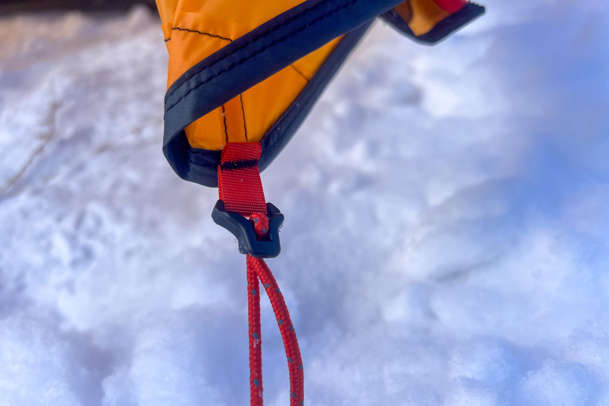 Close-up of a Nemo Kunai 2 tent corner guyline attachment, with durable webbing and tensioners, secured in the snow.