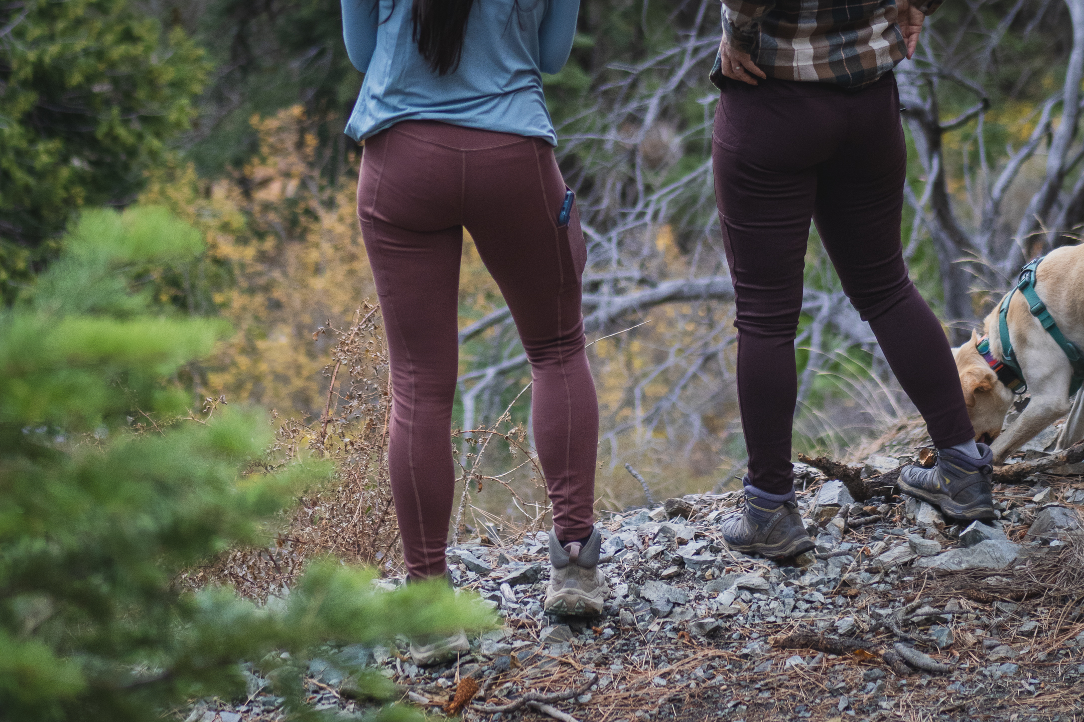 two people standing along a hiking trail, one in pastel pink leggings and another in dark brown leggings.