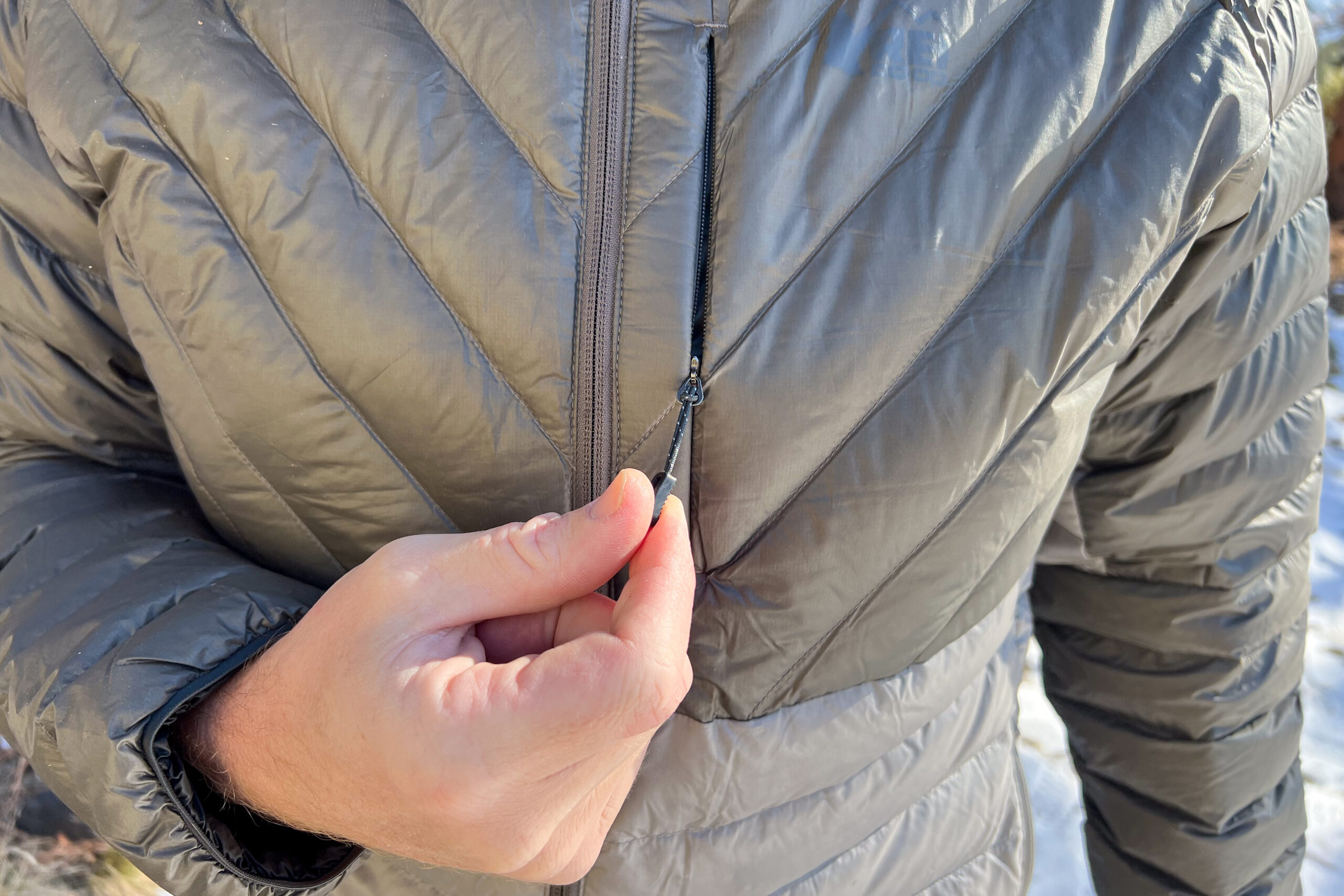 Close-up of a hand adjusting the zippered chest pocket on the REI Magma 850 Down Hoody, showcasing its smooth and durable zipper.