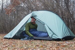 a man in a green jacket sits in a green tent