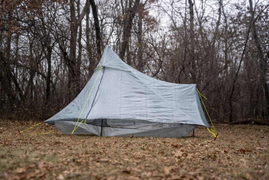 a silver green tent in a forest clearing