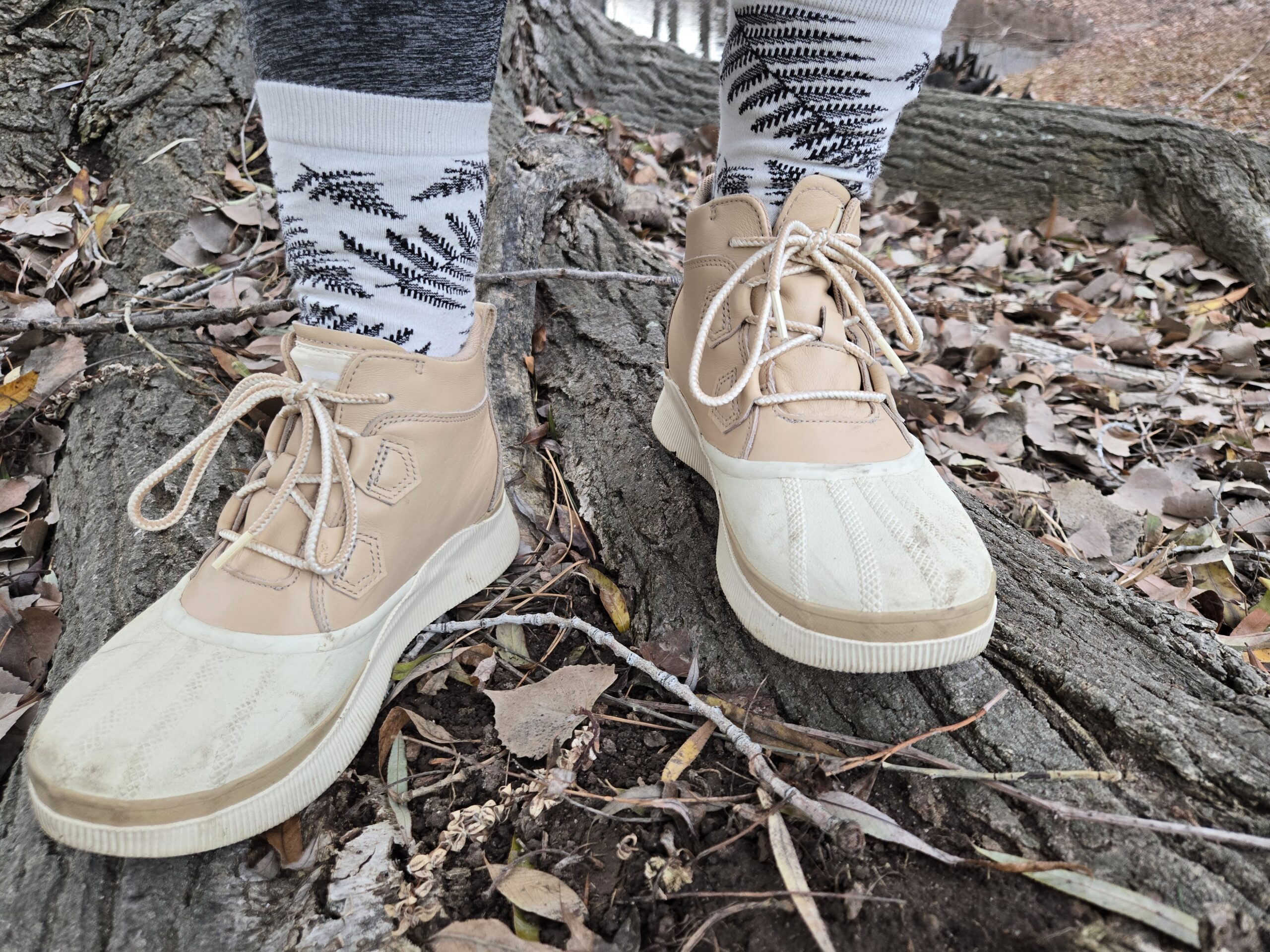 A front view of the creme/beige version of the Sorel Out N About IV boots as someone stands in the leaves.