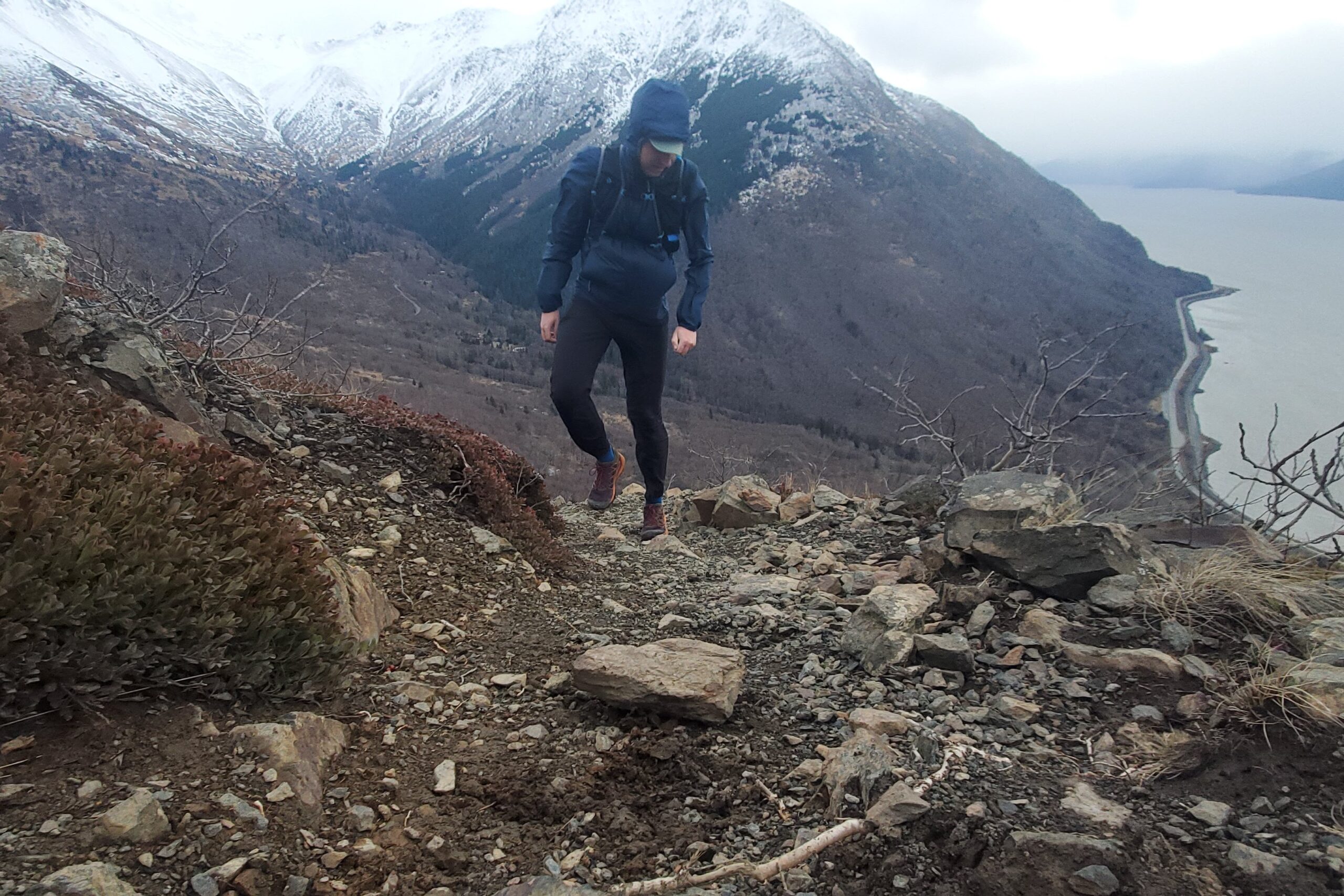 A man hikes up a rocky ridgeline wearing a blue jacket.