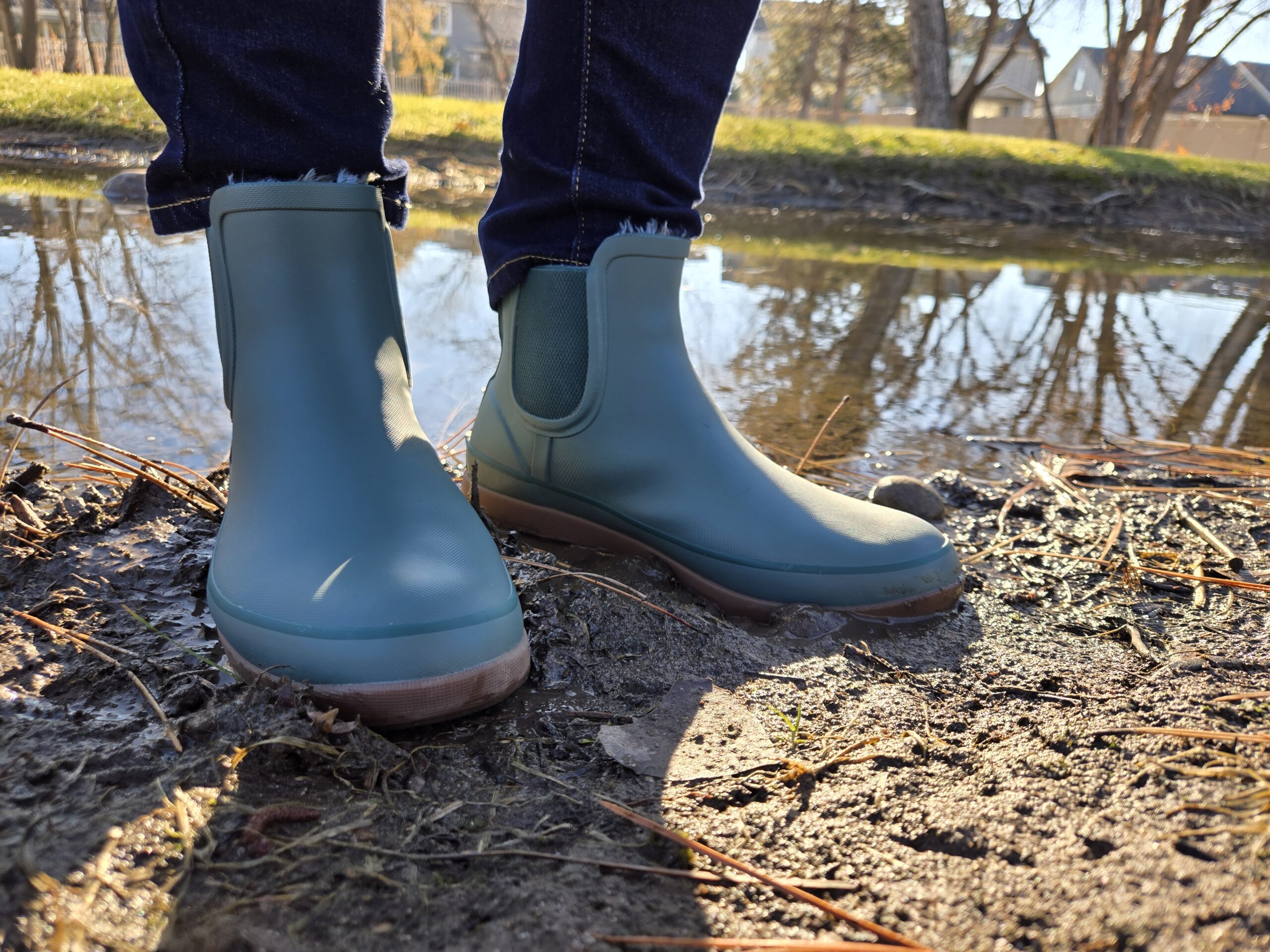 the feet of a women wearing the bogs amanda chelsea rain boots next to a still pond