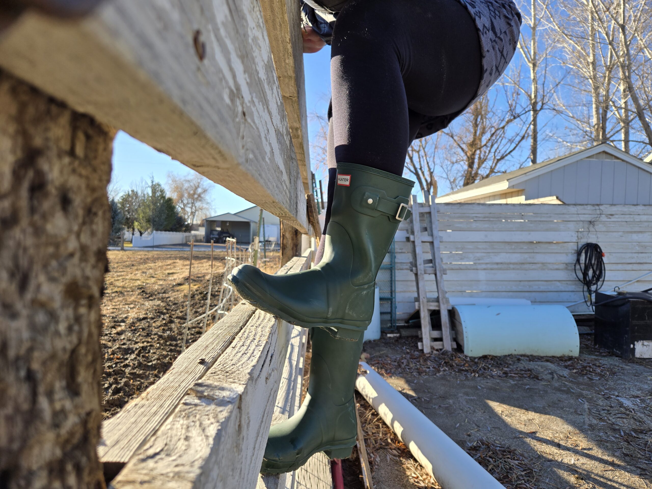 a women climbing a horse paddock fence in hunter rain boots