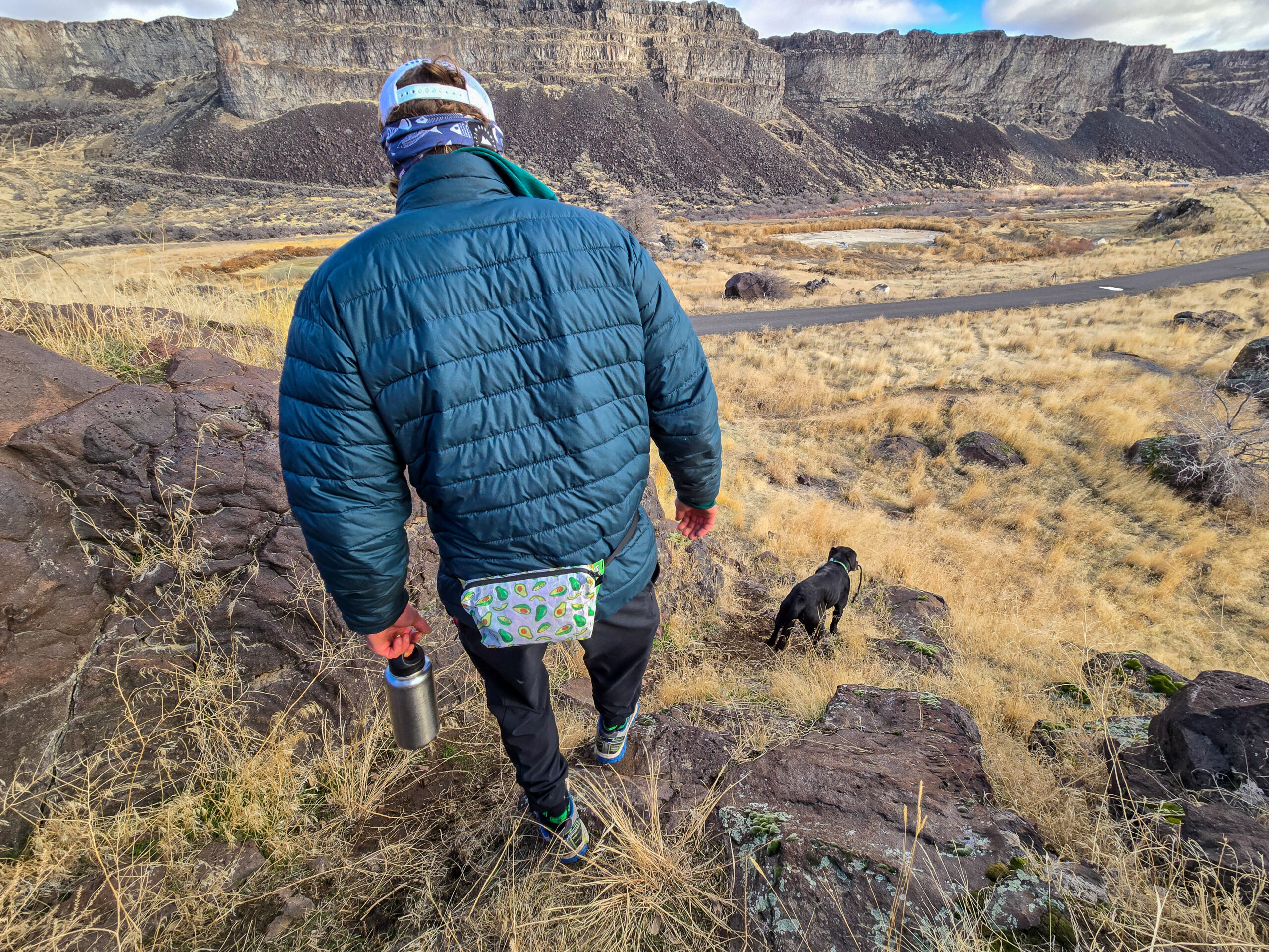 a man walking down some desert hillside in a canyon landscape with his dog wearing a high tail designs fanny pack on his lumbar