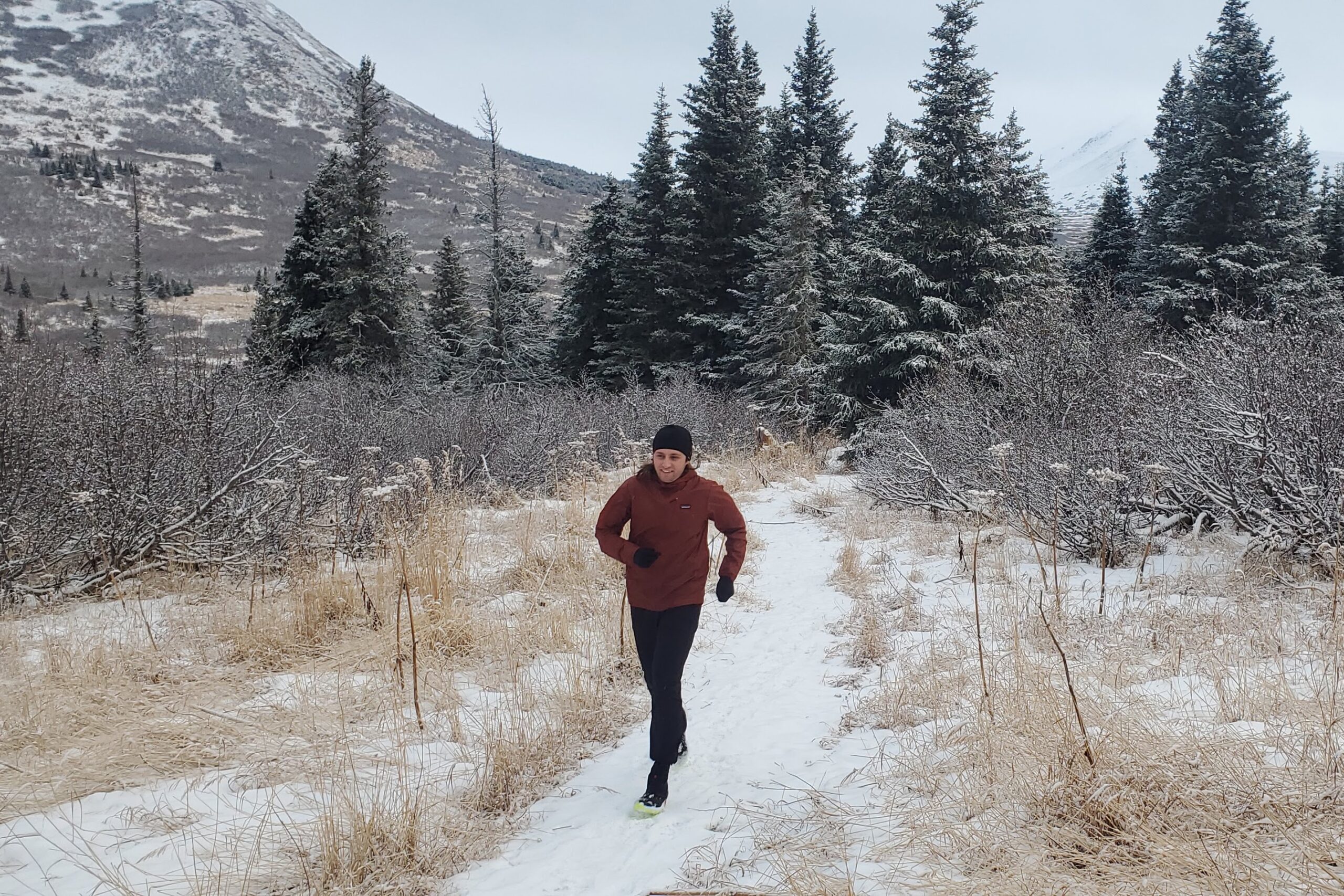A man runs along a snow covered trail with mountains in the background.