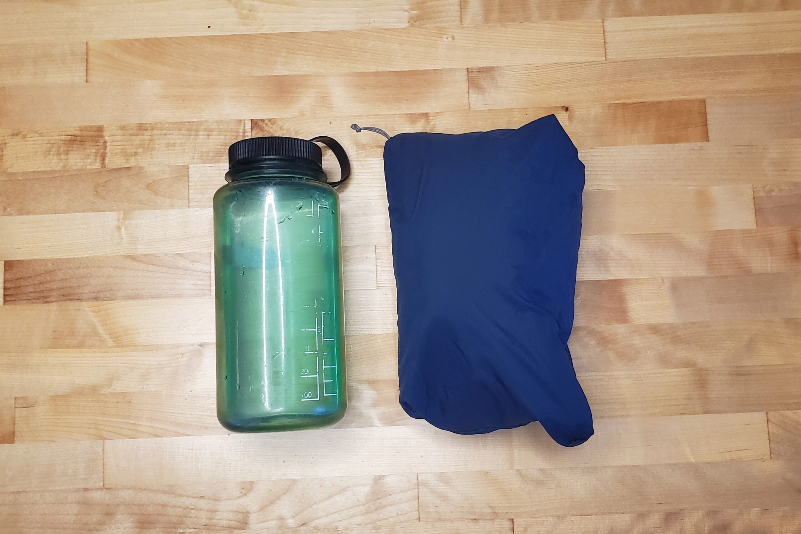 A jacket is bundled up to show it's size relative to a one liter water bottle.