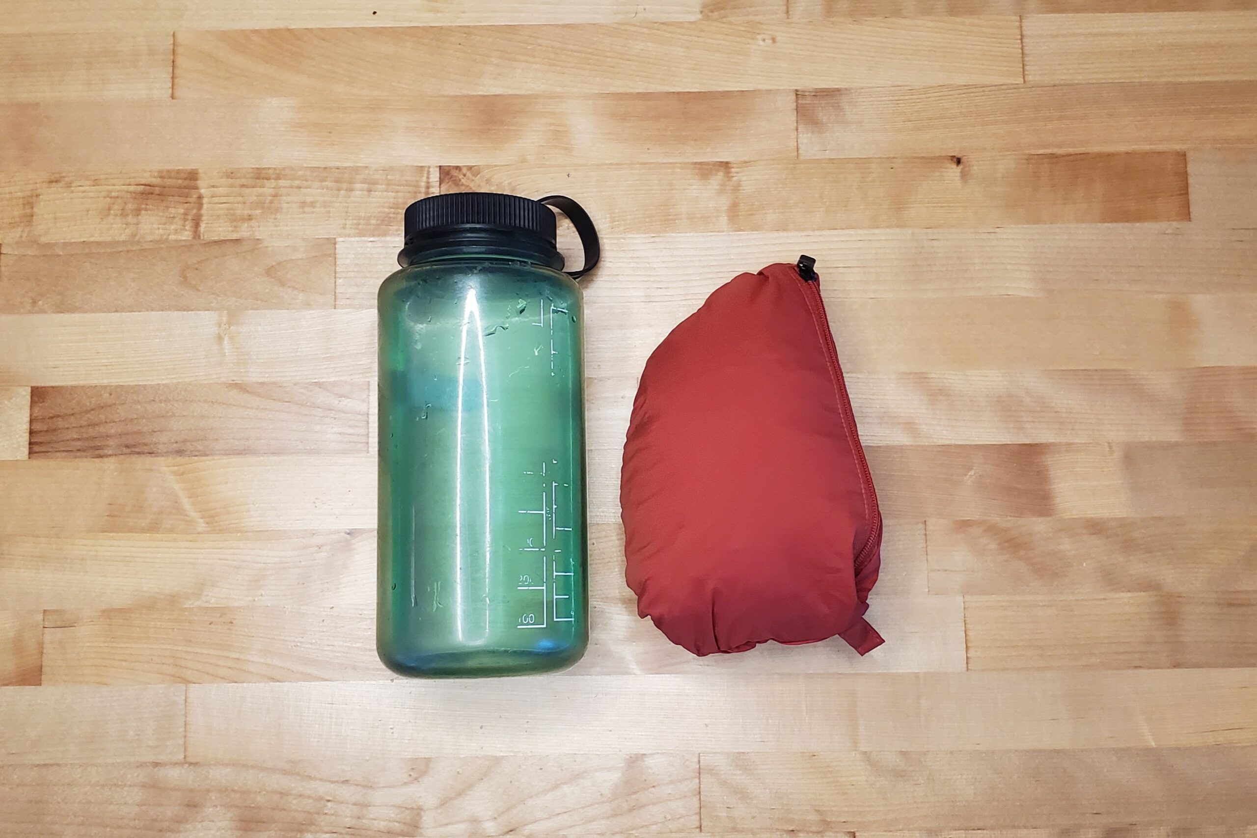 A jacket packed into a ball next to a one liter water bottle.