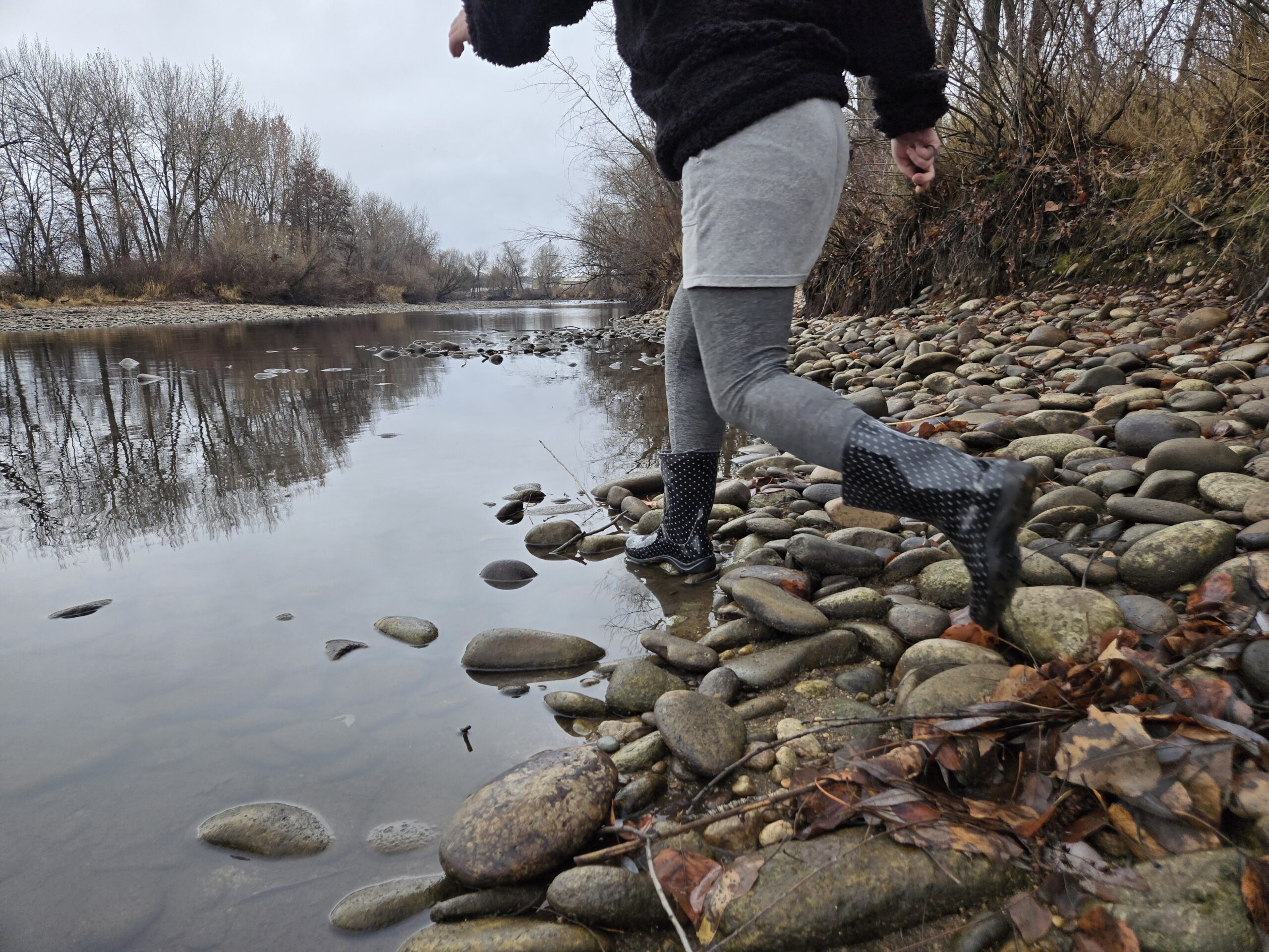 a woman wearing the sloggers rain and garden boot next to a still river with river rock on the edge
