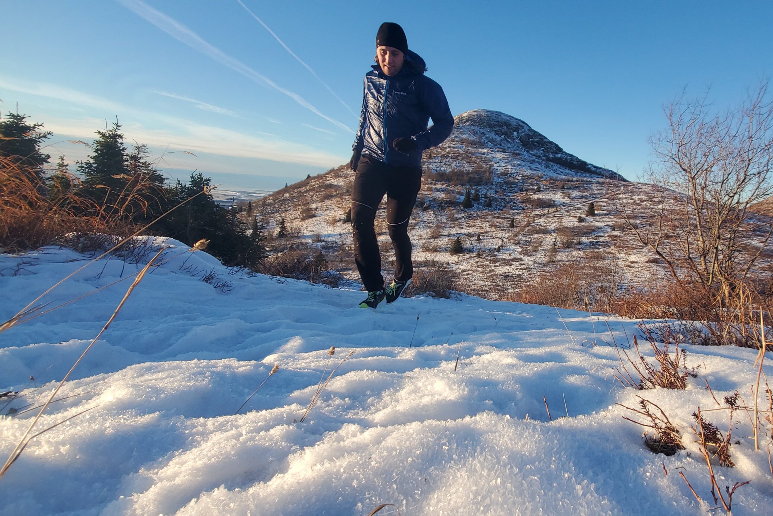 A man runs up a snowy hill with a ridgeline in the background.