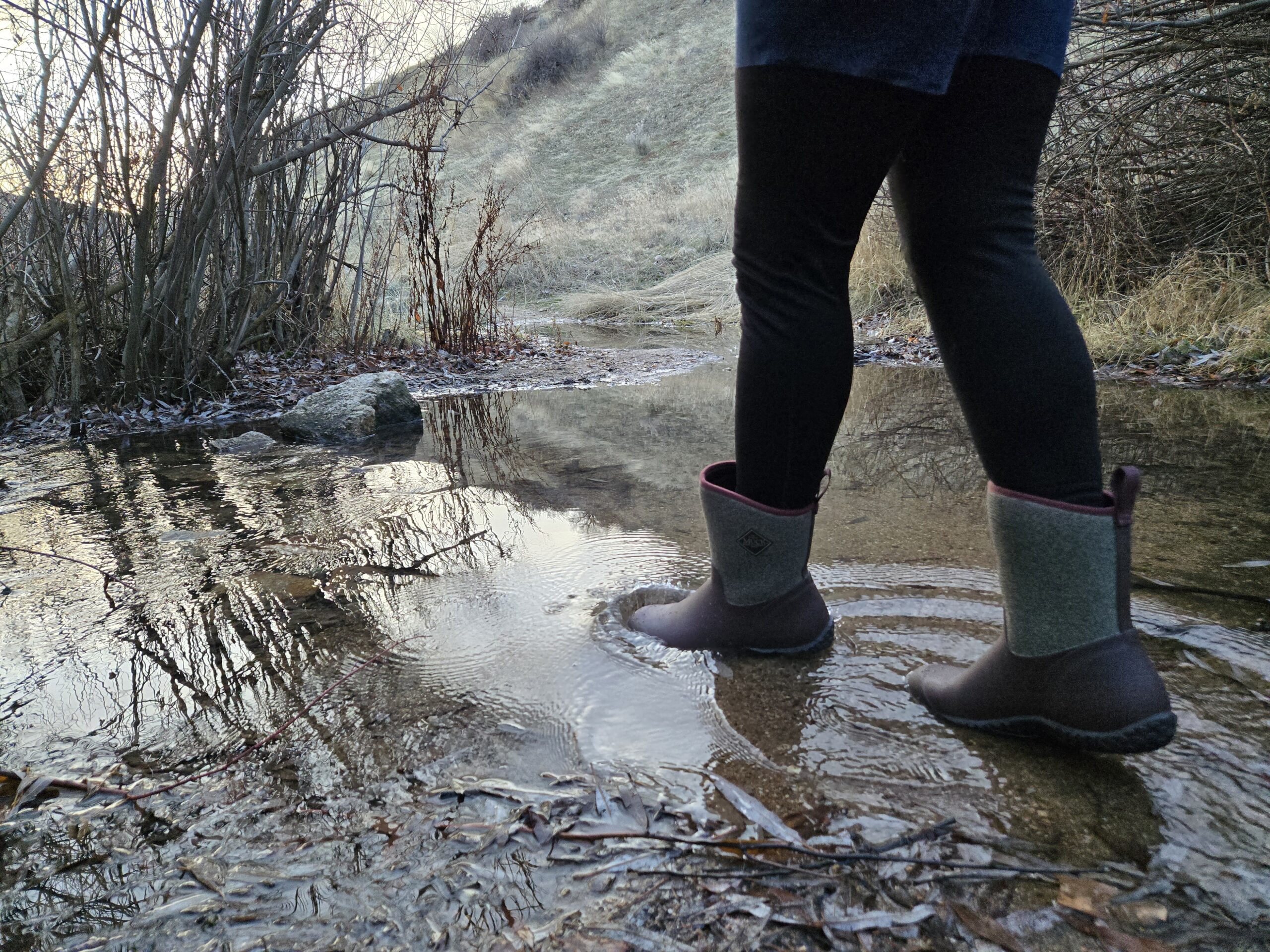 woman walking in a creek wearing muck boots