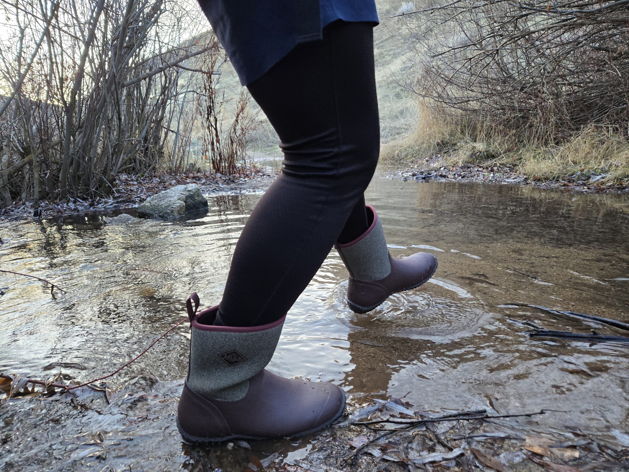 person walking across a creek in muck boots mucksters mid II