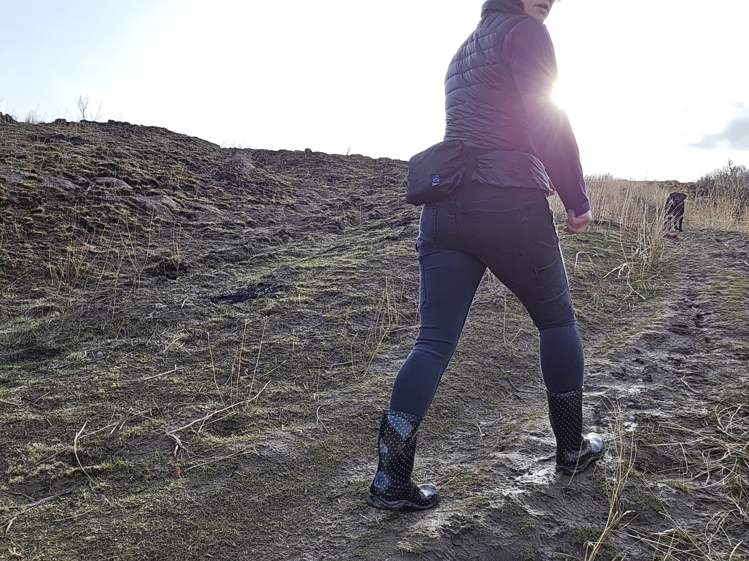 woman walking up a muddy trail with her dog at sunset