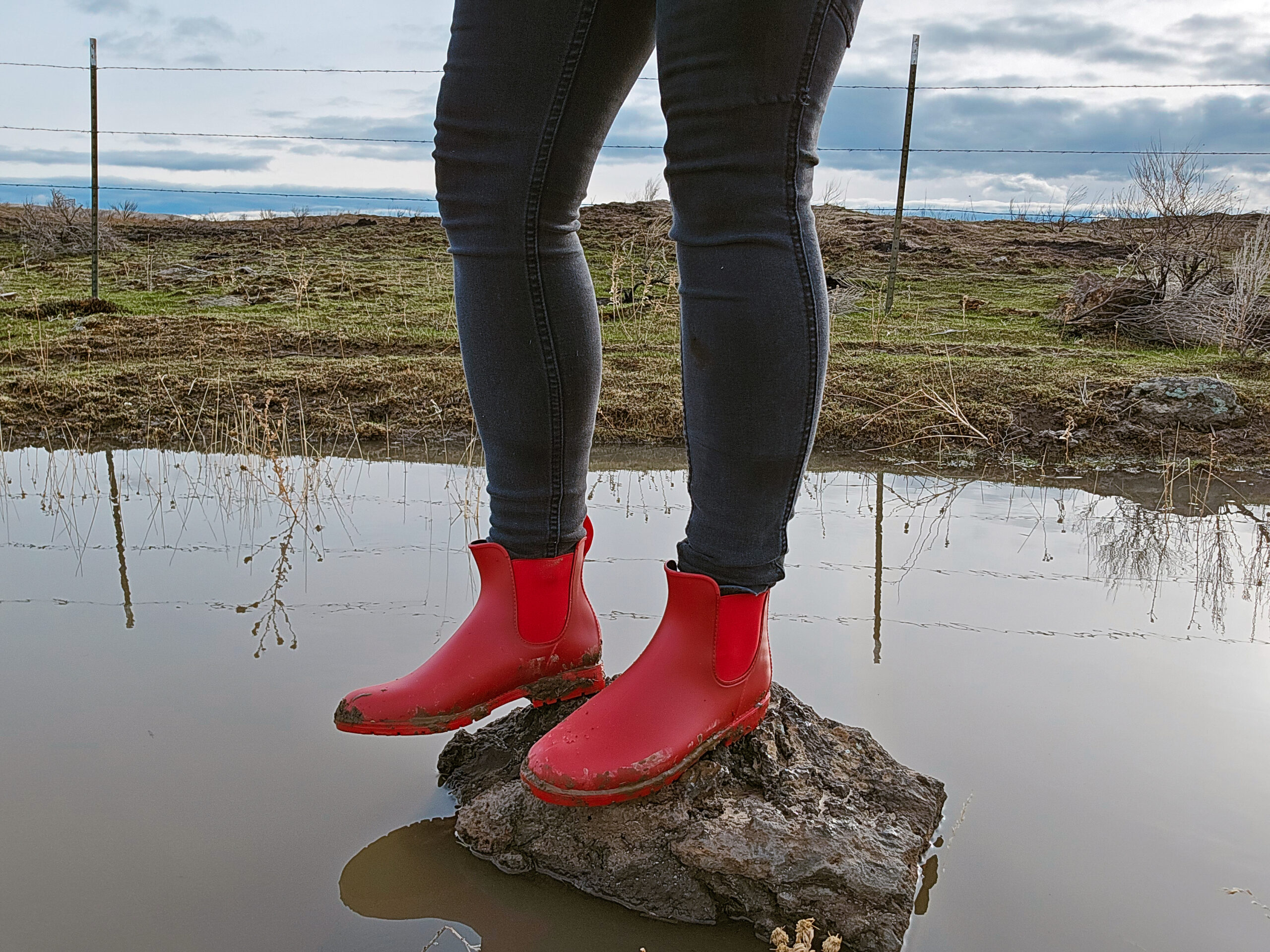 woman standing on a small rock surrounded by water. she's wearing the asgard chelsea boots
