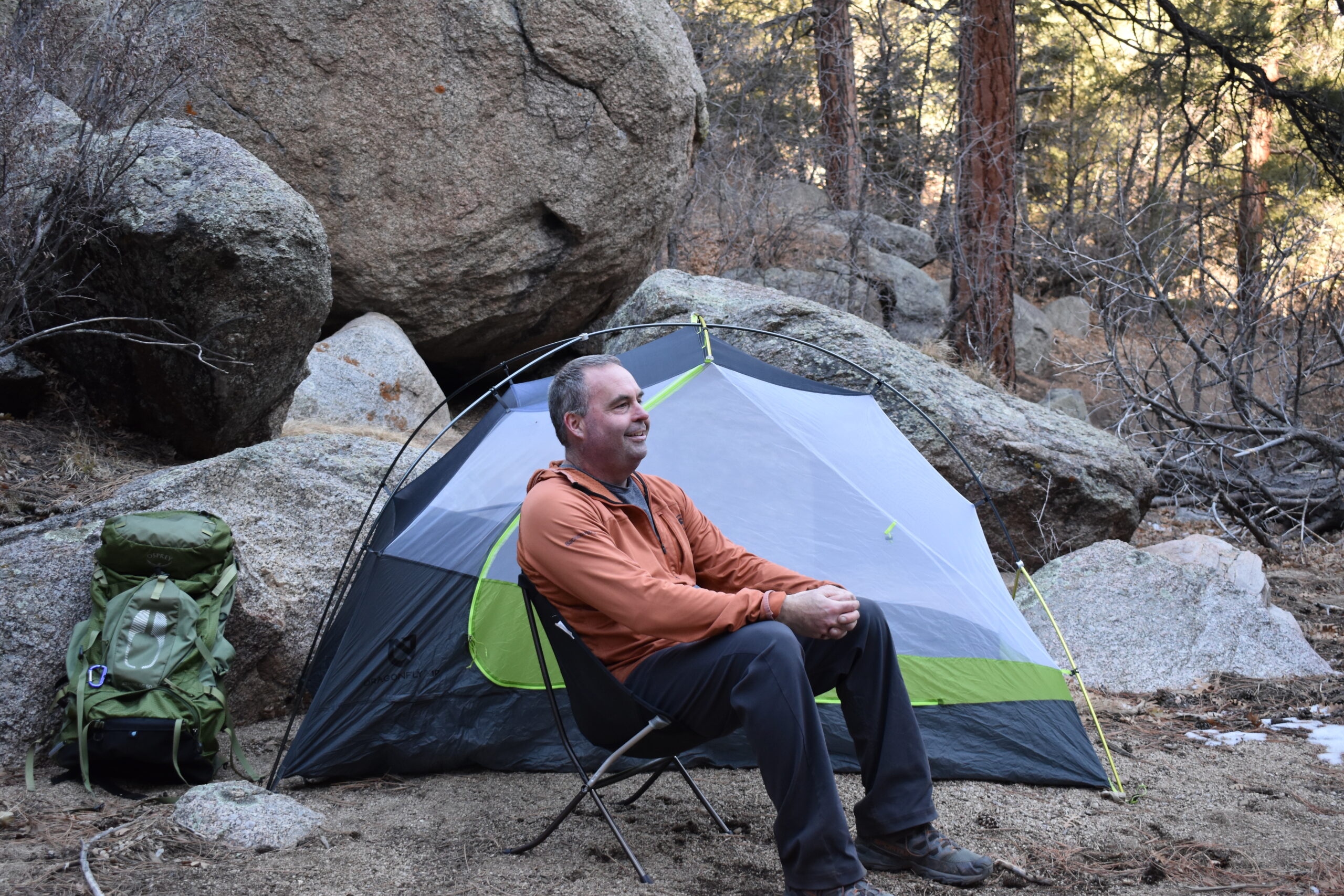 A backpacker sits on the Skyline Chair in front of his tent at a desert canyon campsite surrounded by huge boulders