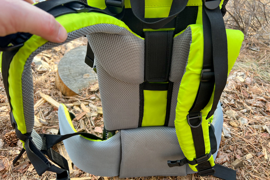 Close-up of padded shoulder straps and back support of a bright green child carrier, highlighting the breathable mesh material.