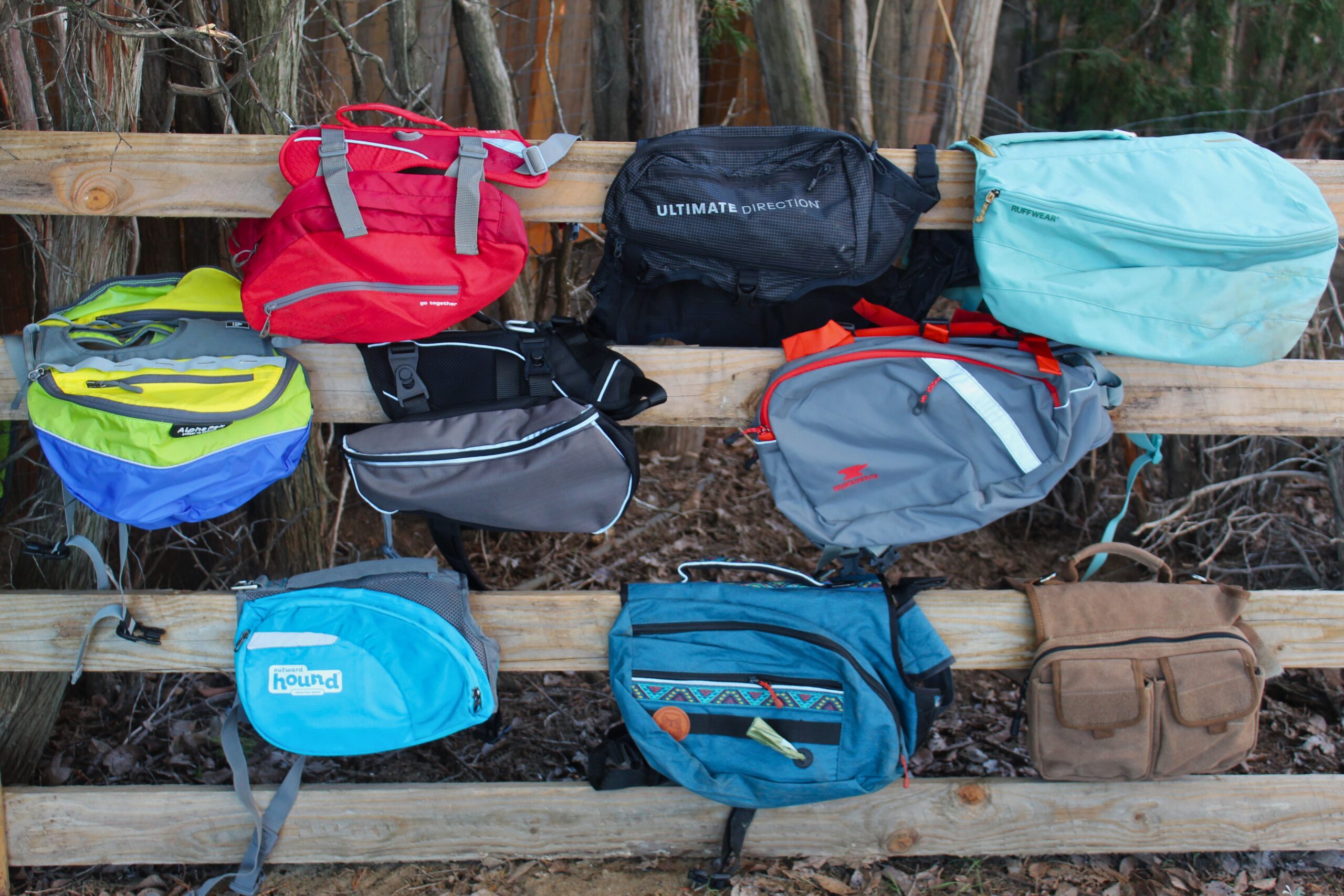 Nine dog backpacks hanging on a fence