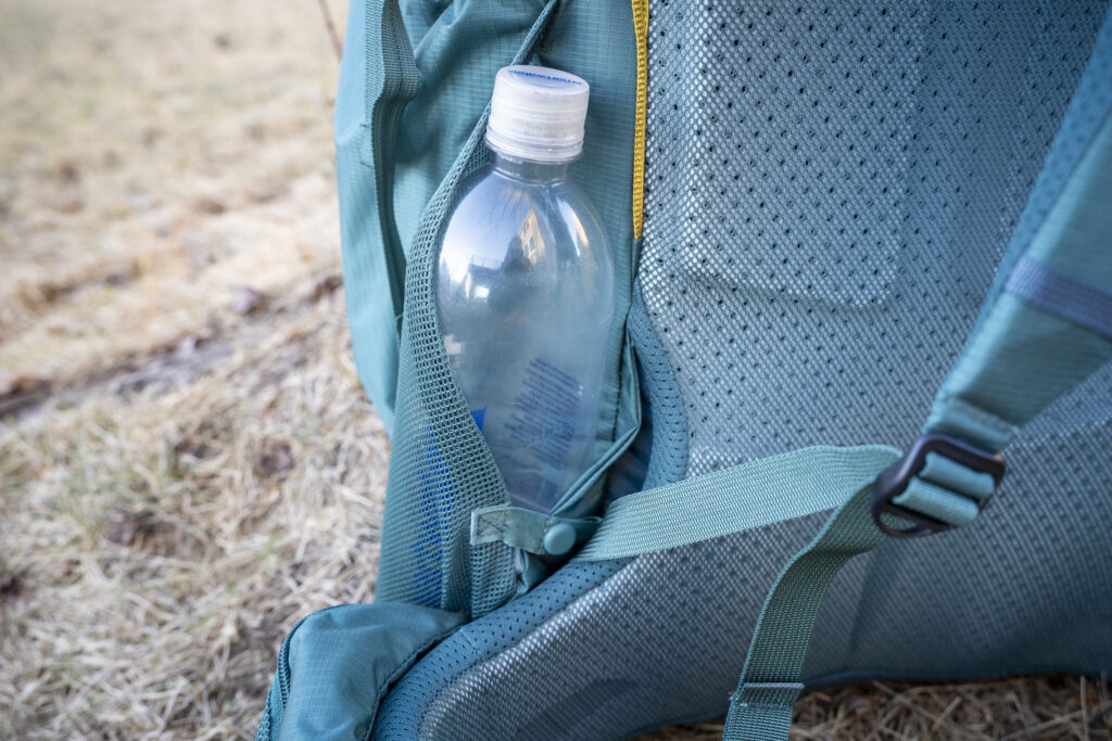 a water bottle rests in a pocket on the side of a backpack