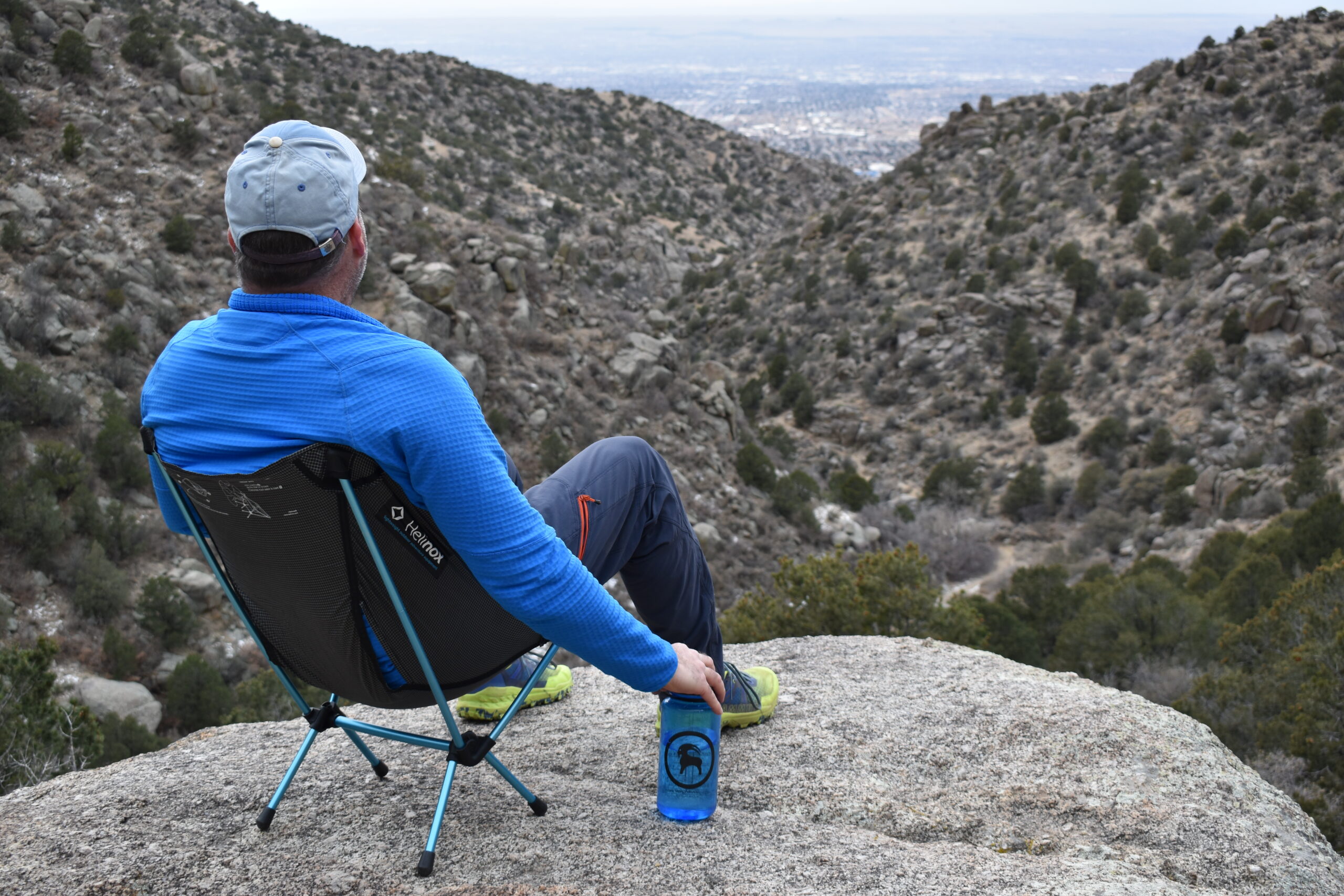 A hiker sits on the Helinox Chair Zero on a rocky cliff looking down a desert canyon