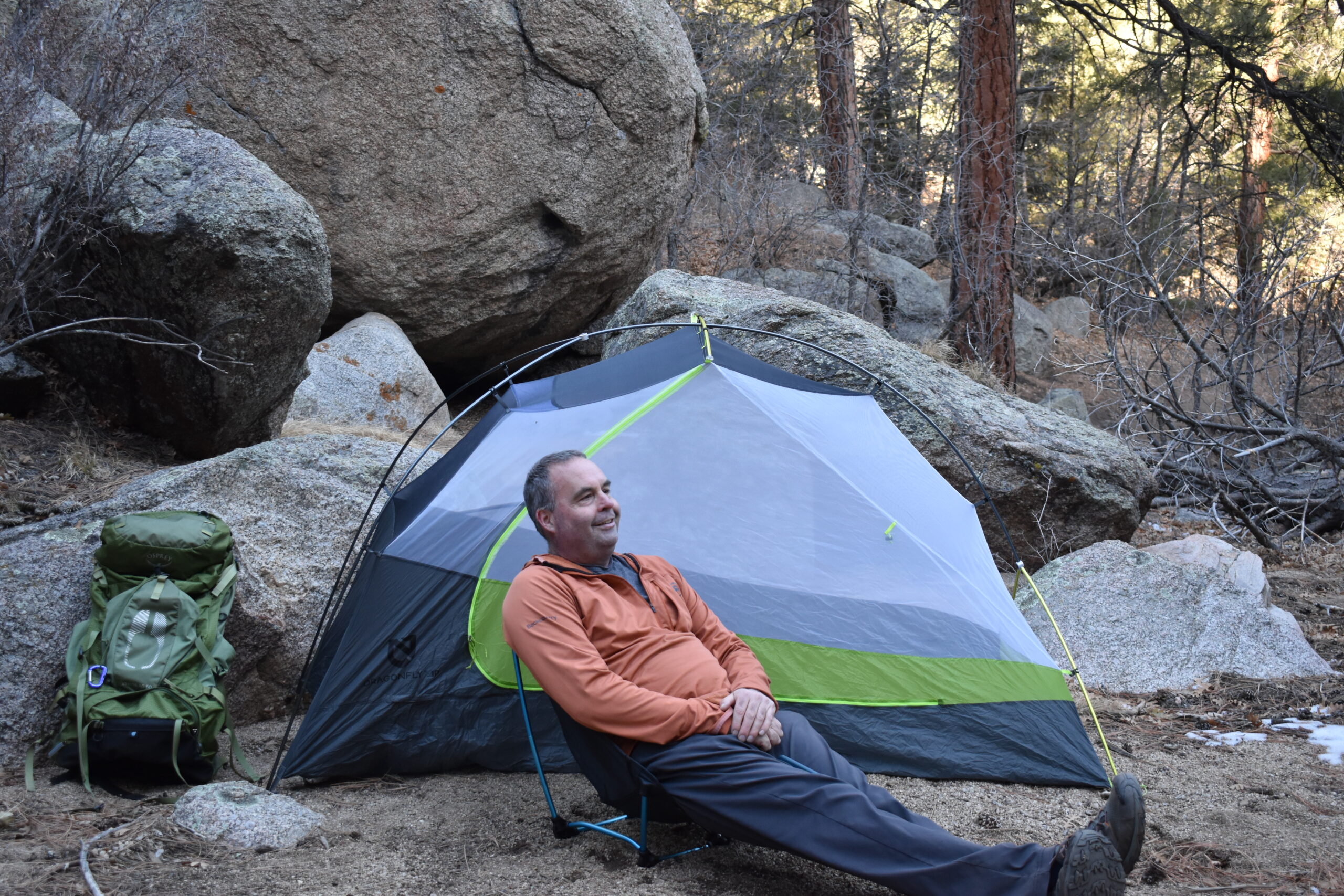Male hiker sitting on a backpacking chair in front of his tent and giant boulders at a campsite in a high desert canyon
