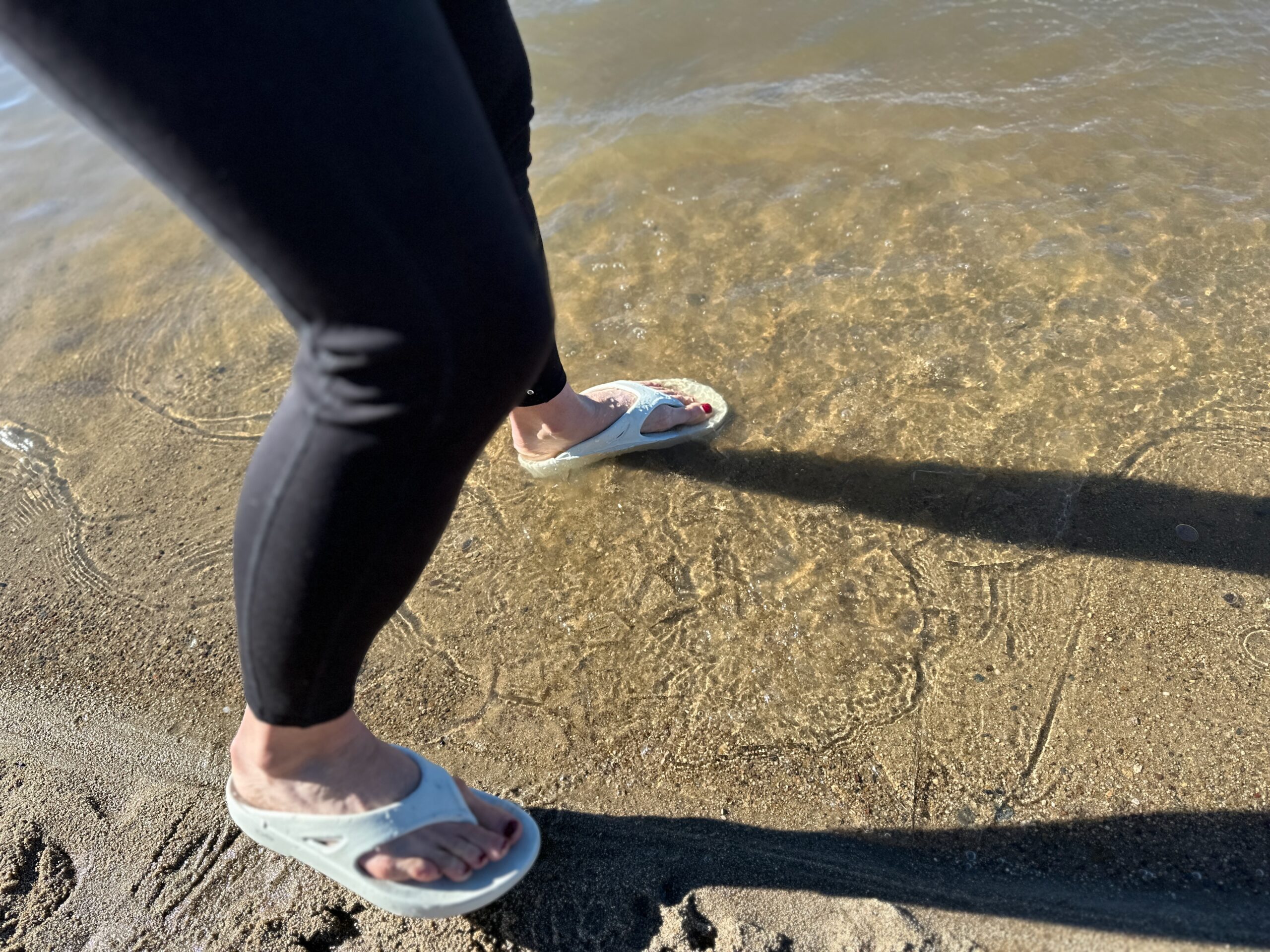 the OOfos OOriginals shoe splashing in water at a sandy lakeshore