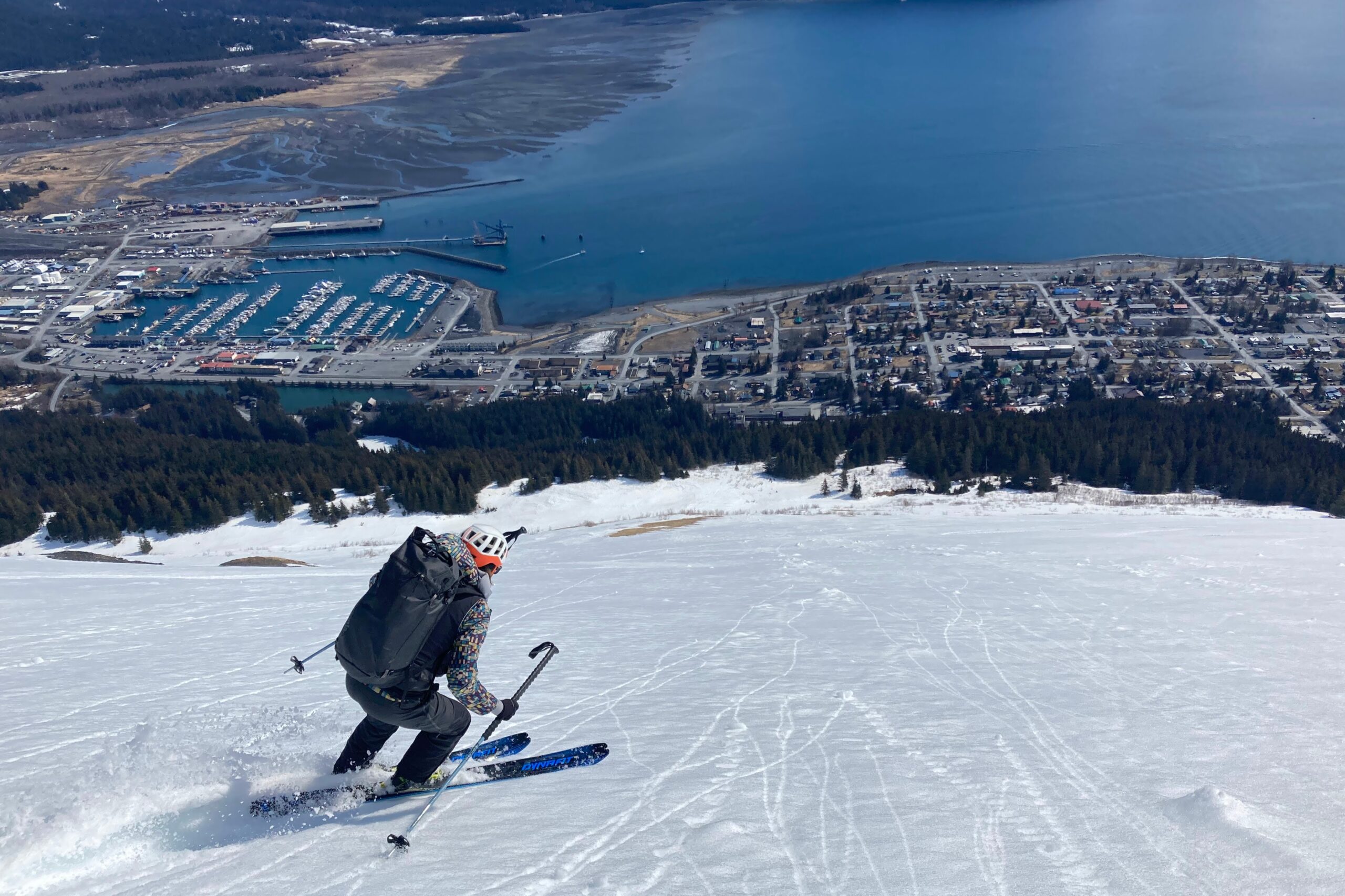 A man skis down a slope above a small town along the ocean.