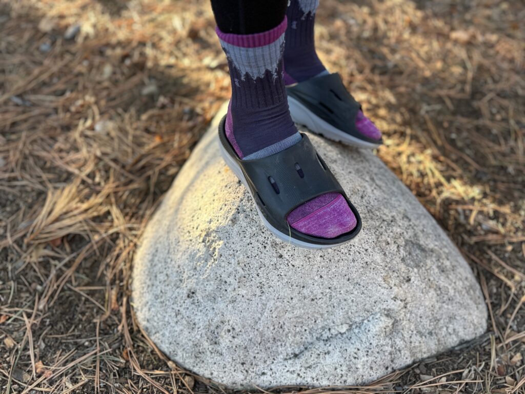 a woman wears the HOKA ORA Recovery 3 Slides while standing on a rock