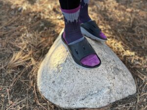 a woman wears the HOKA ORA Recovery 3 Slides while standing on a rock