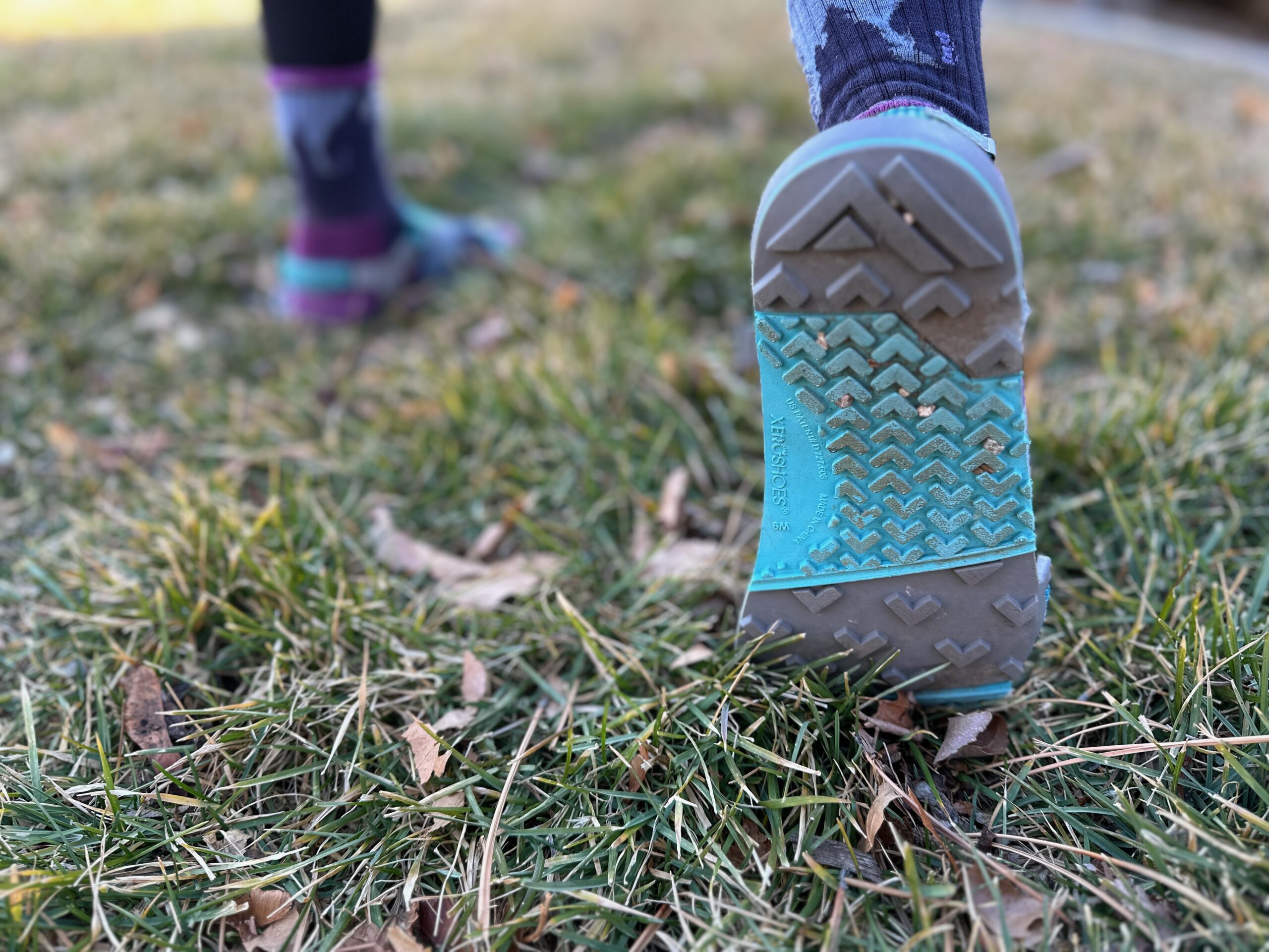 a woman shows off the soles of the Xero Shoes Z-Trail EV on grass
