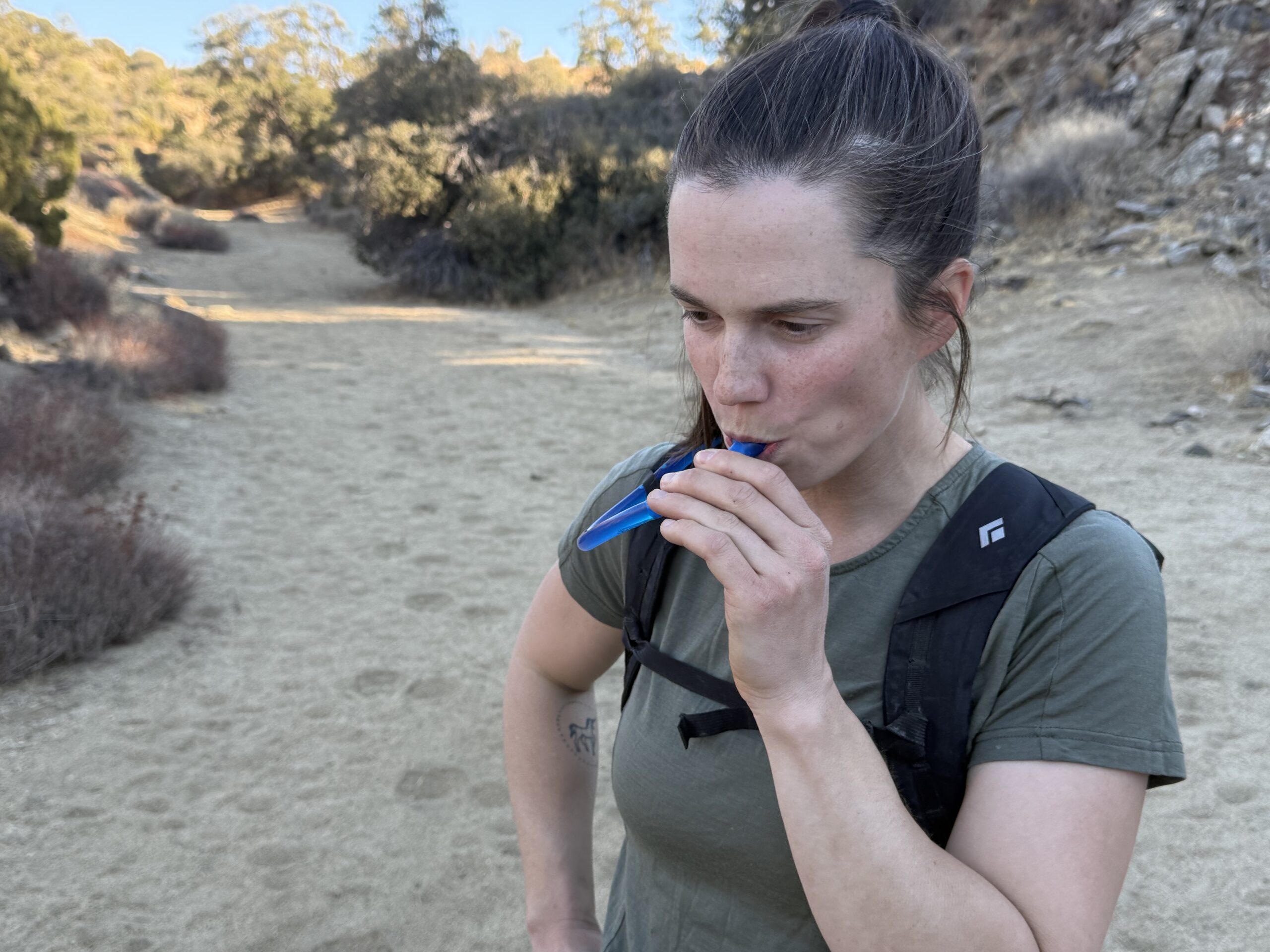 Hiker drinks from a hydration hose in a sandy wash
