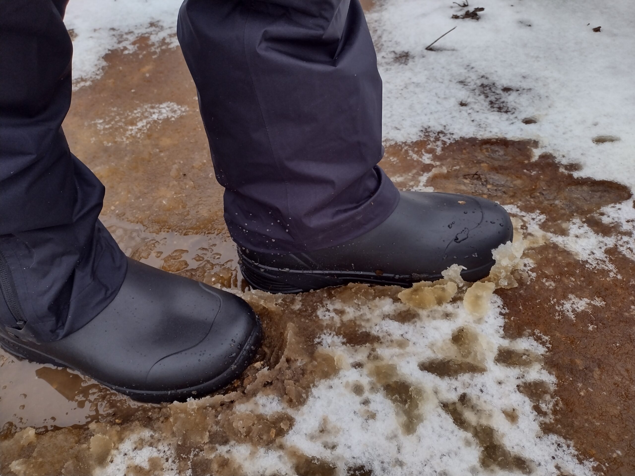 Ground level view of someone wearing the black Bozeman Mid boots in muddy snow.