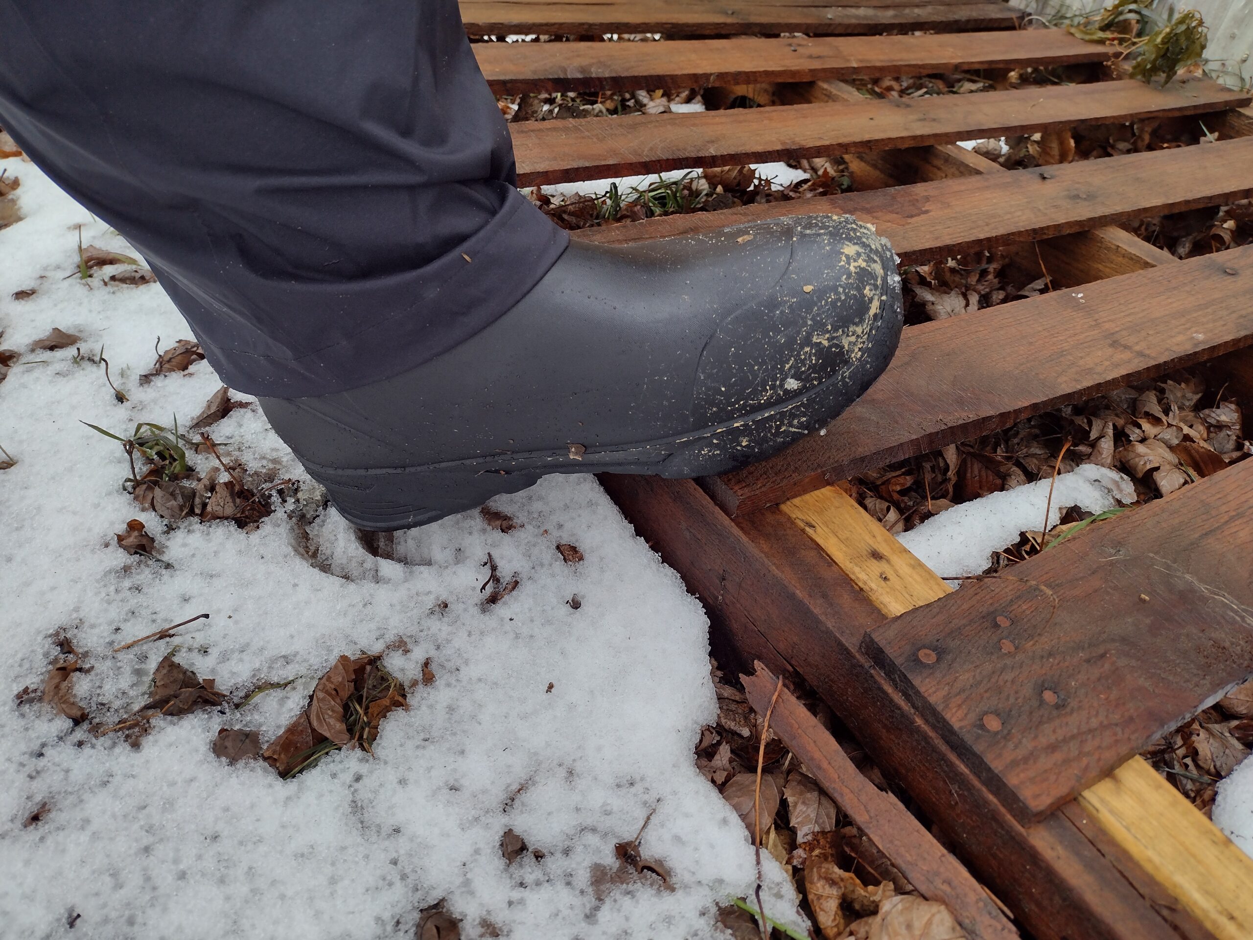 Ground level view of someone wearing the black Bozeman Mid boots stepping onto a pallet.