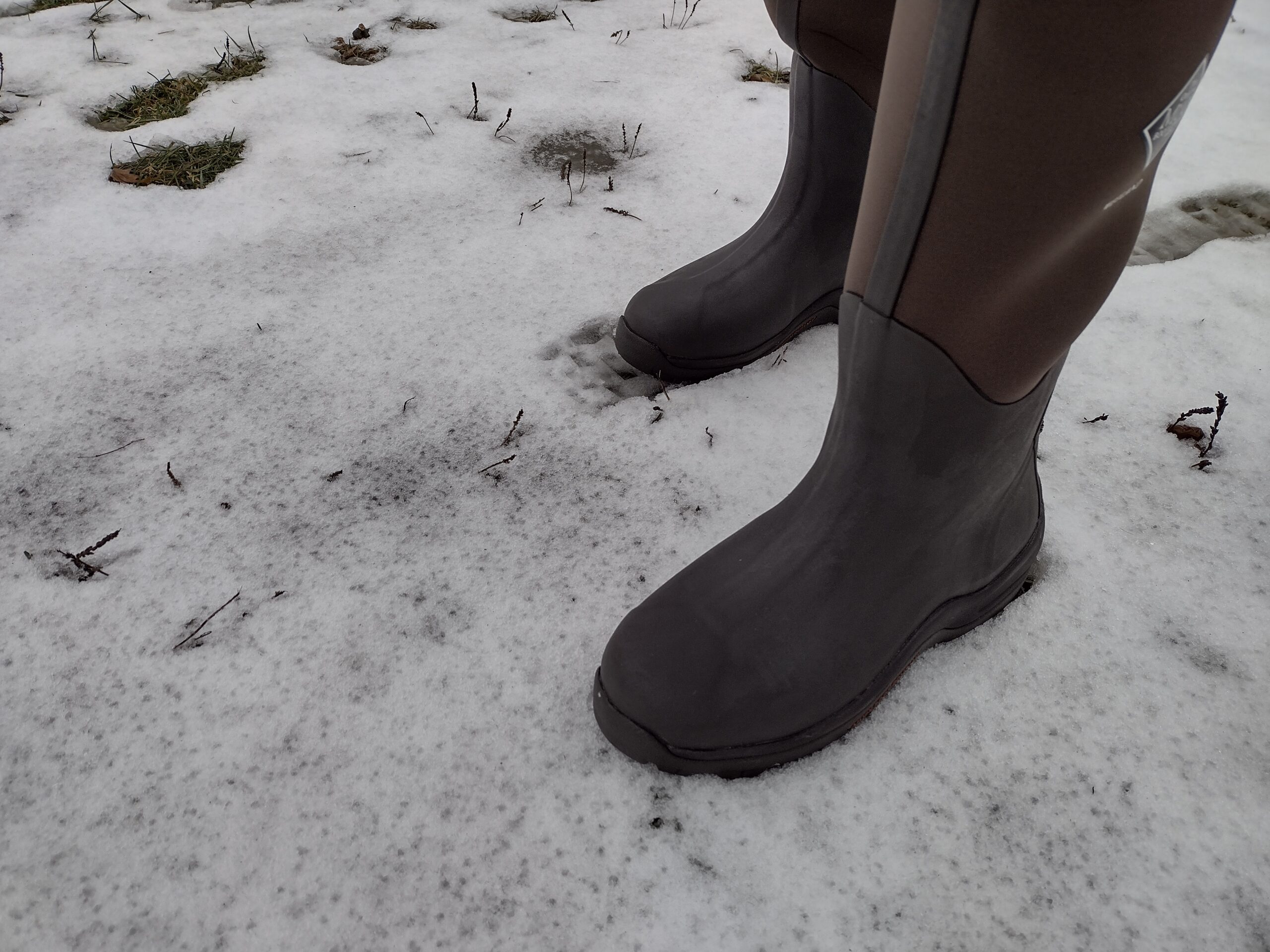 Ground level view of someone wearing the brown Original Muck Boot Wetland standing in the snow.