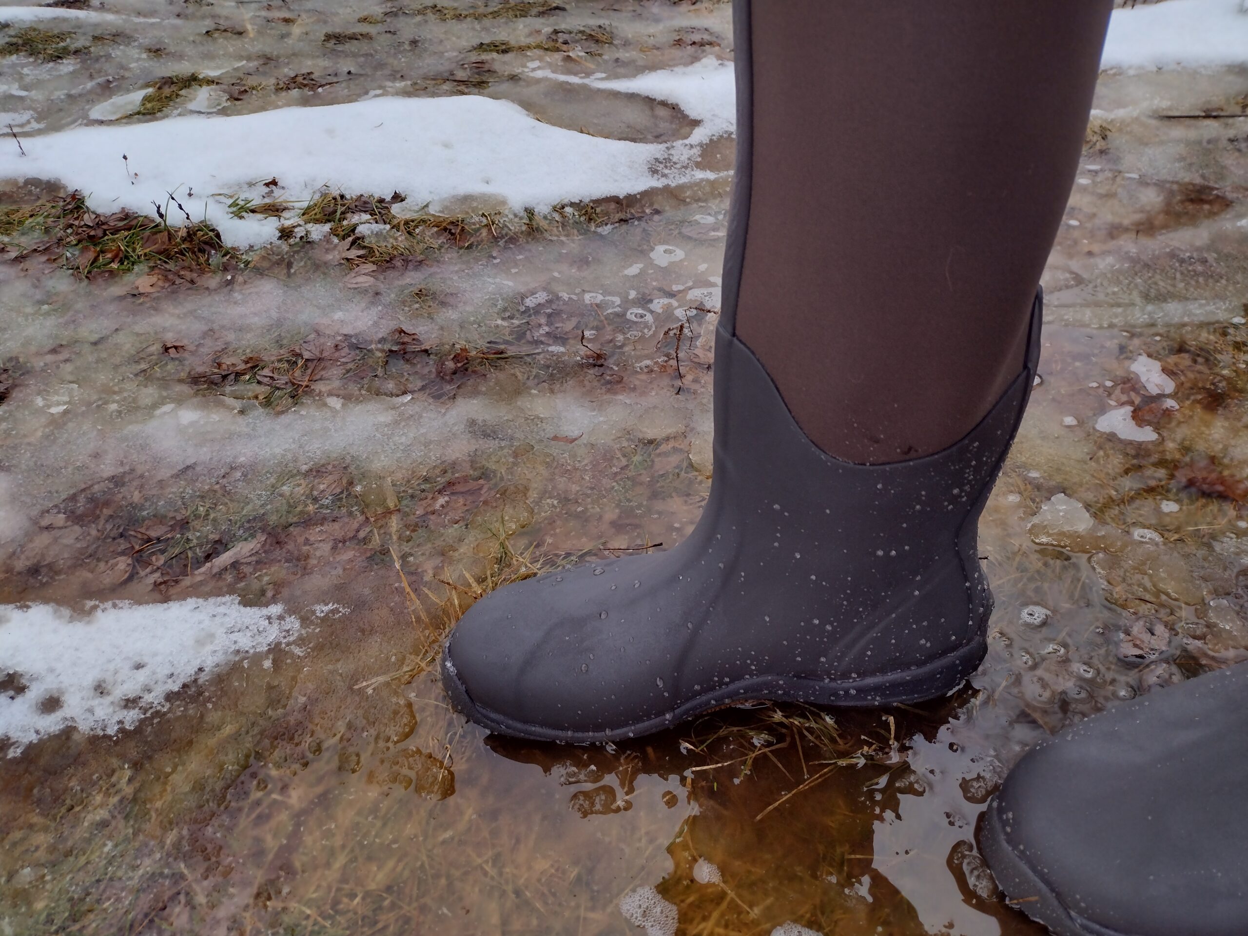 Ground level view of someone wearing the brown Original Muck Boot Wetland standing in water.