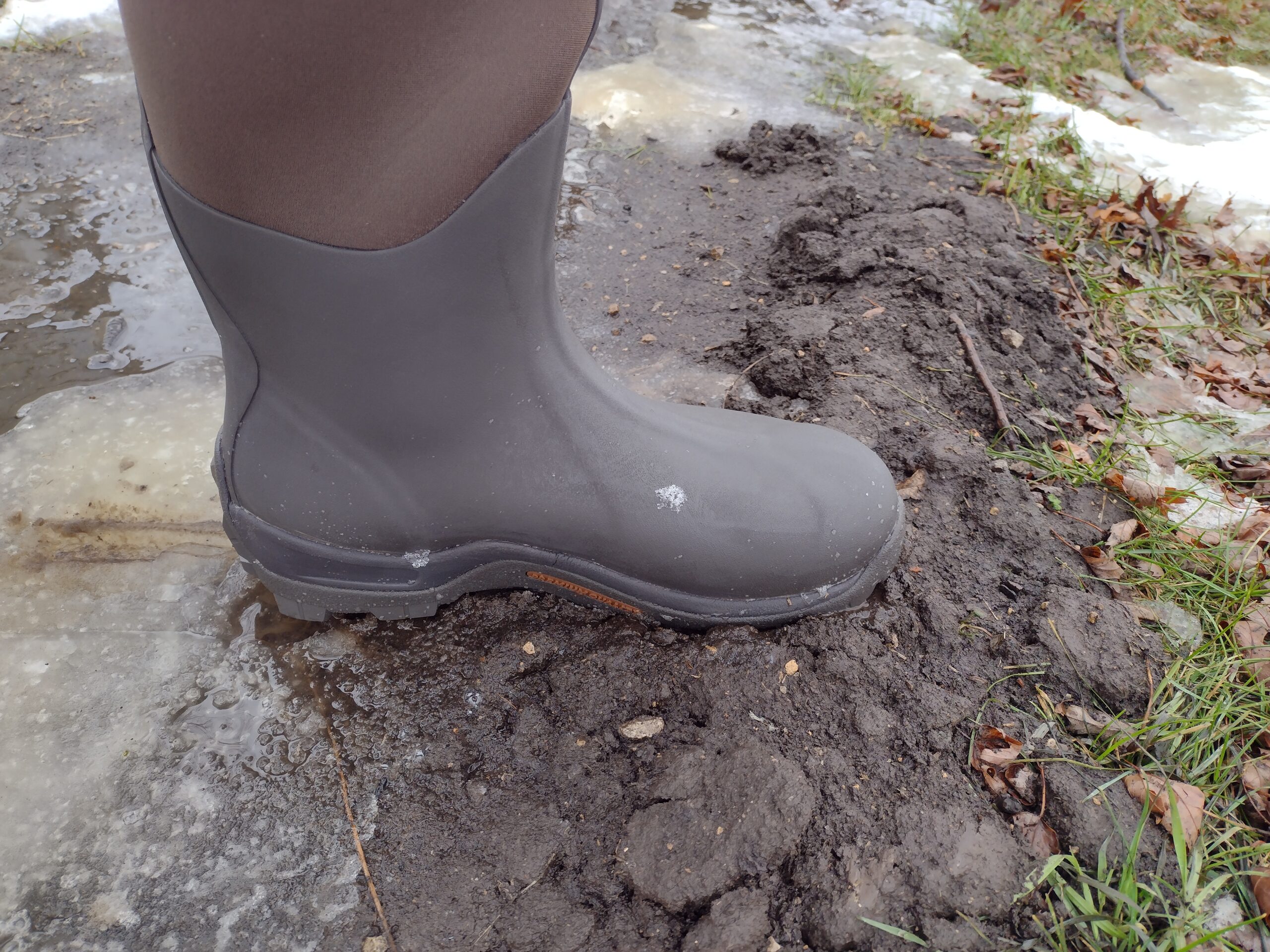 Ground level view of someone wearing the brown Original Muck Boot Wetland standing in mud.