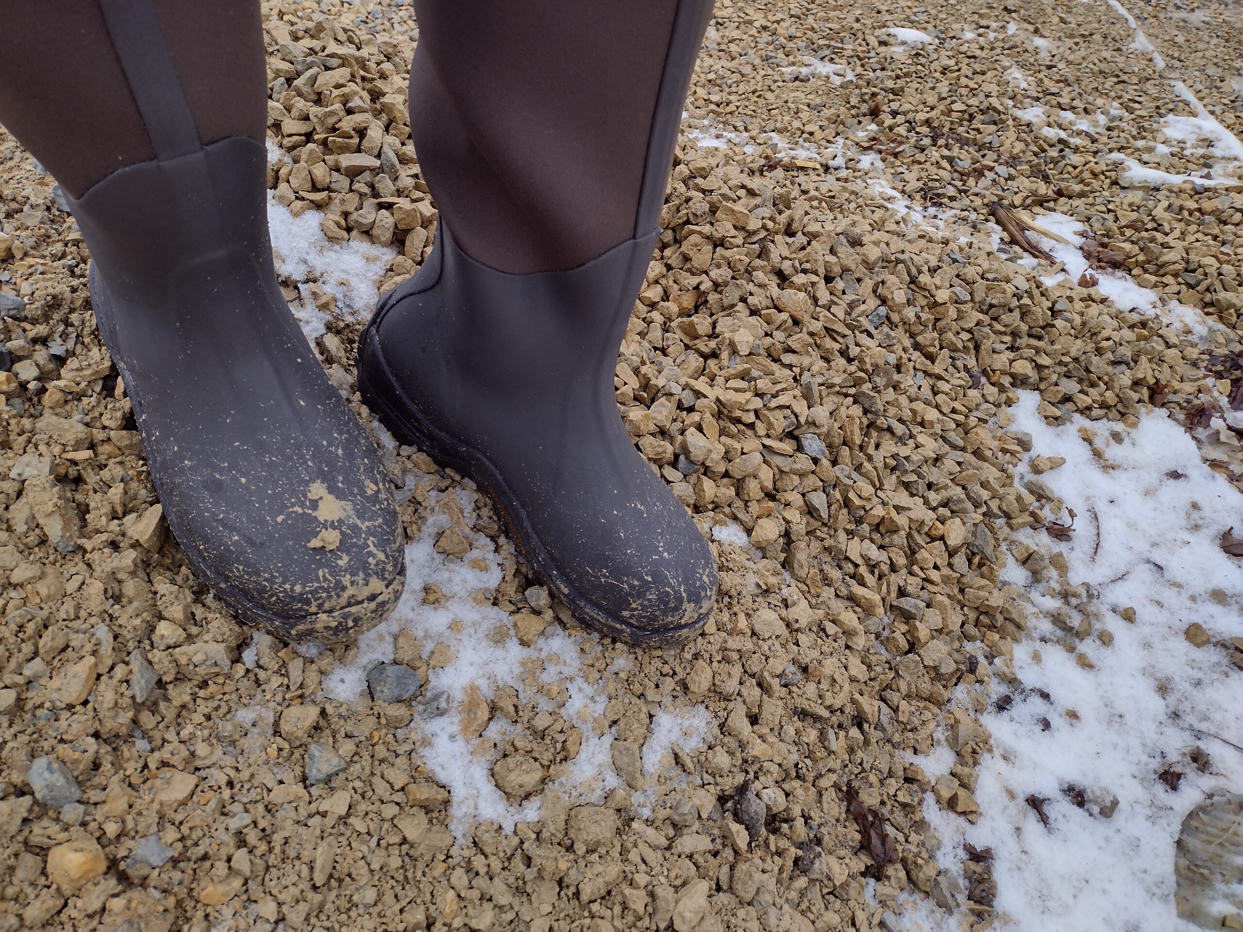 Ground level view of someone wearing the brown Original Muck Boot Wetland standing on a gravel pile.