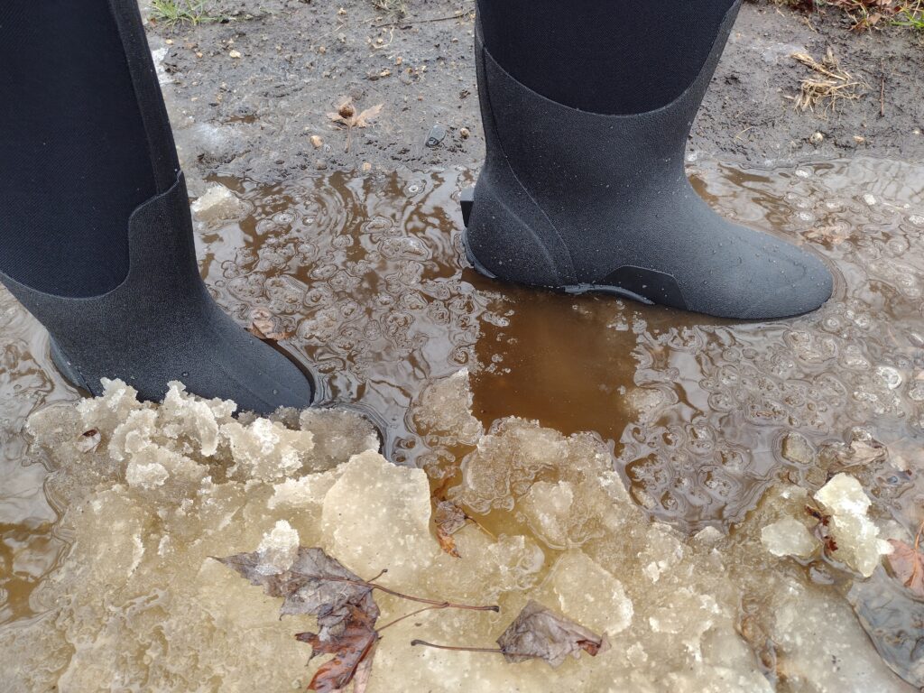 Ground level view of someone wearing the black Bogs Classic High standing in icy water.