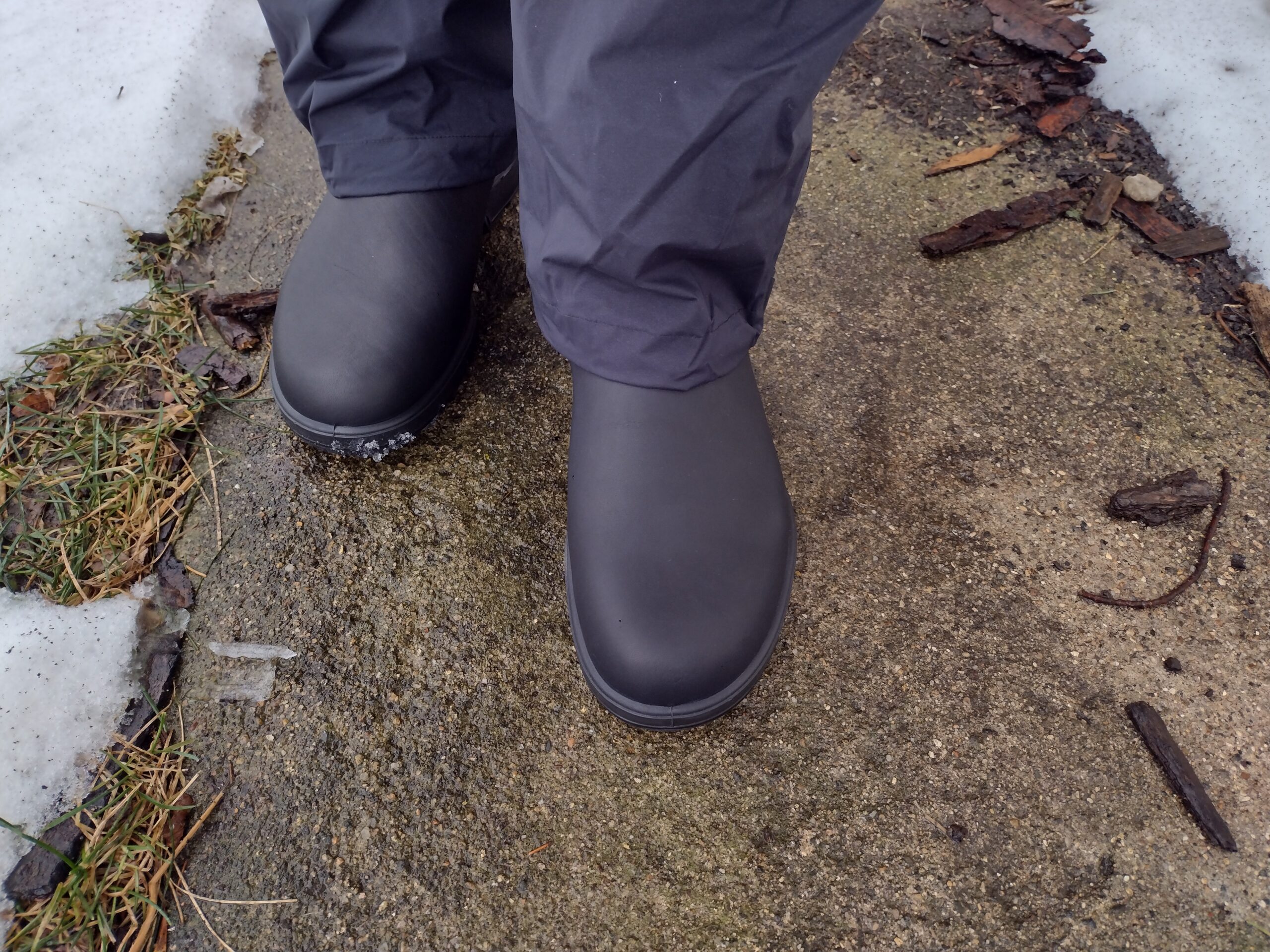 Ground level view of someone wearing the black Blundstone Original Chelsea standing on a wet sidewalk.