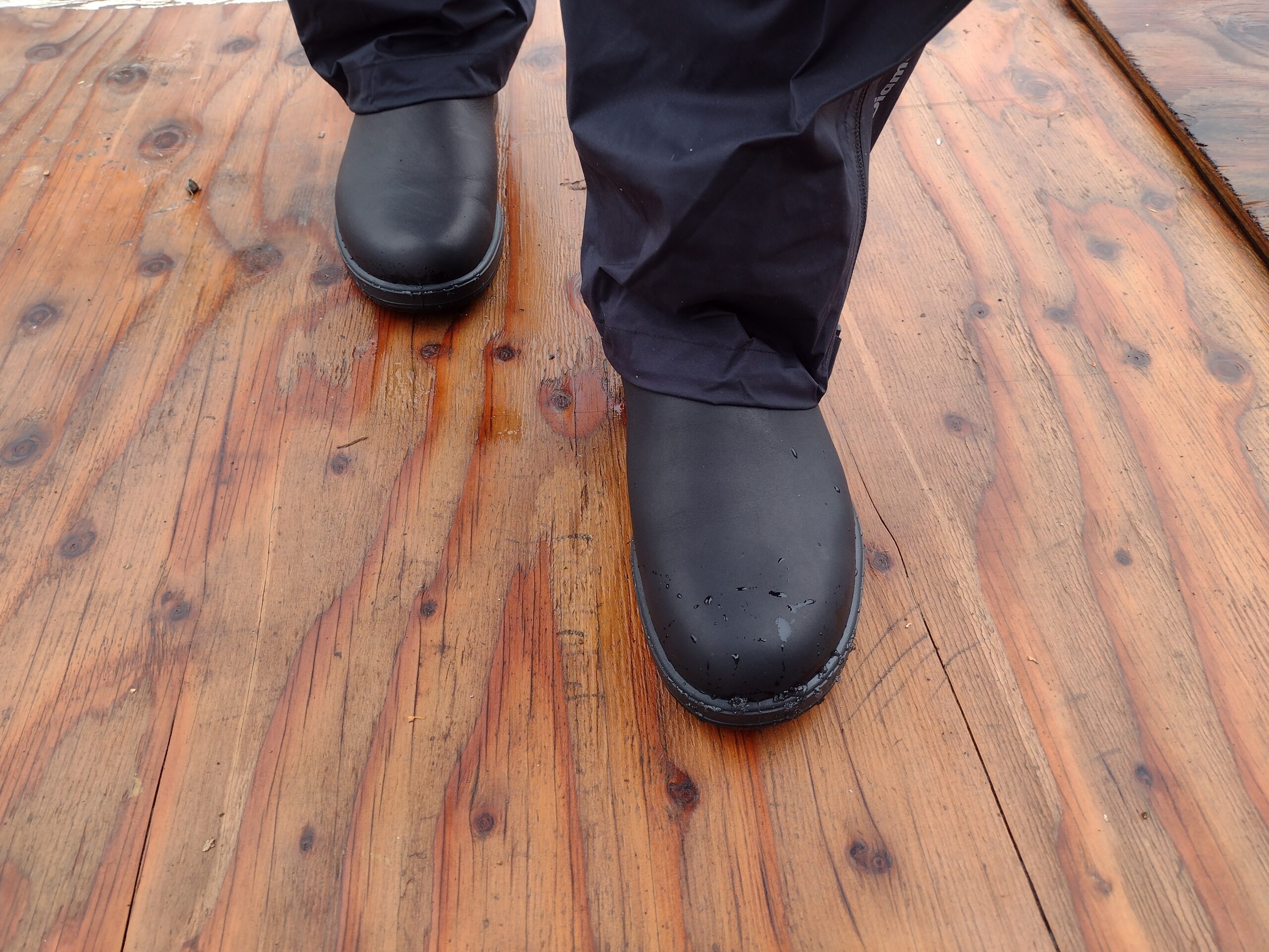 Ground level view of someone wearing the black Blundstone Original Chelsea standing on a wet wood surface.