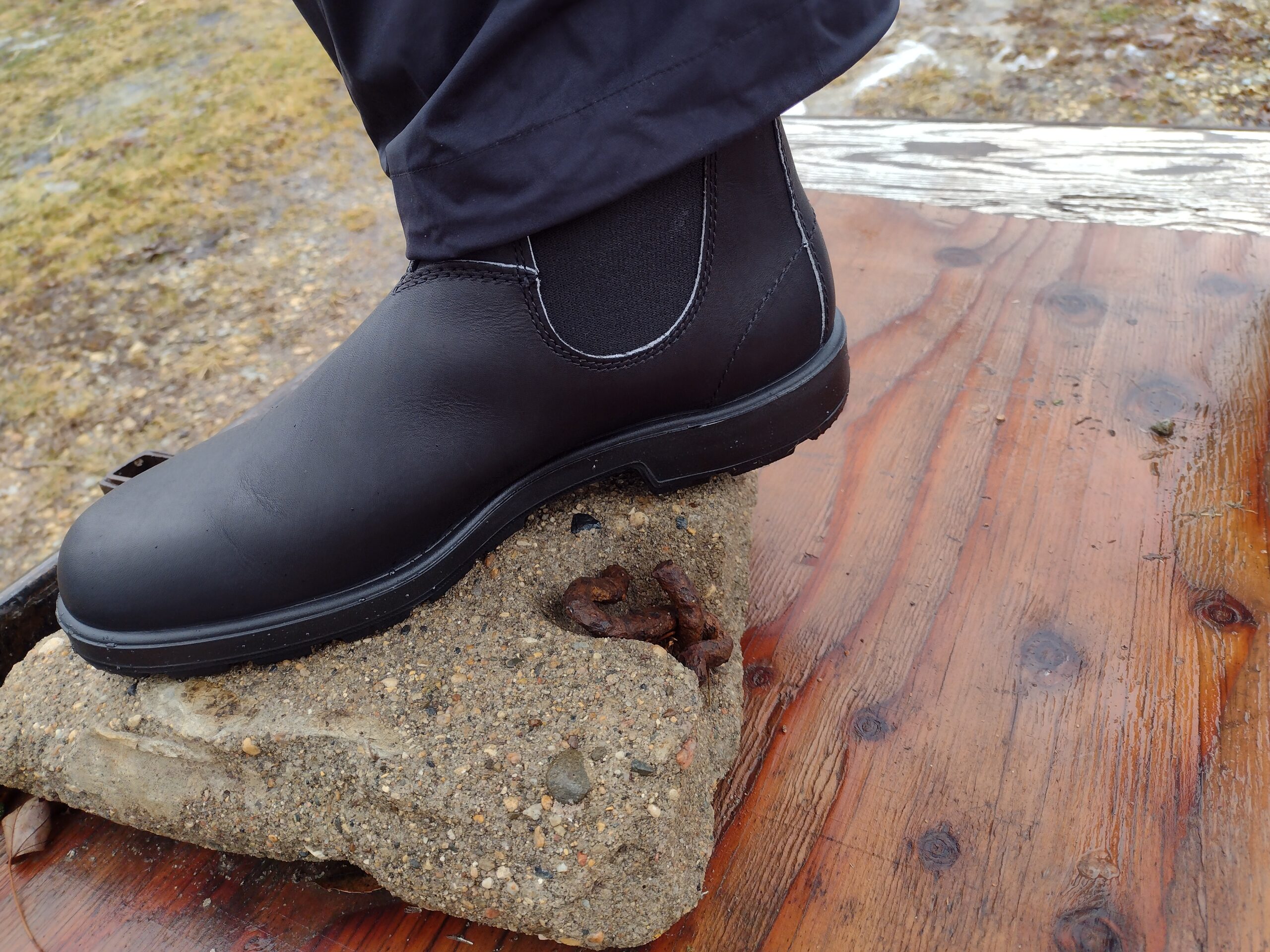 Ground level view of someone wearing the black Blundstone Original Chelsea standing on a wet rock.