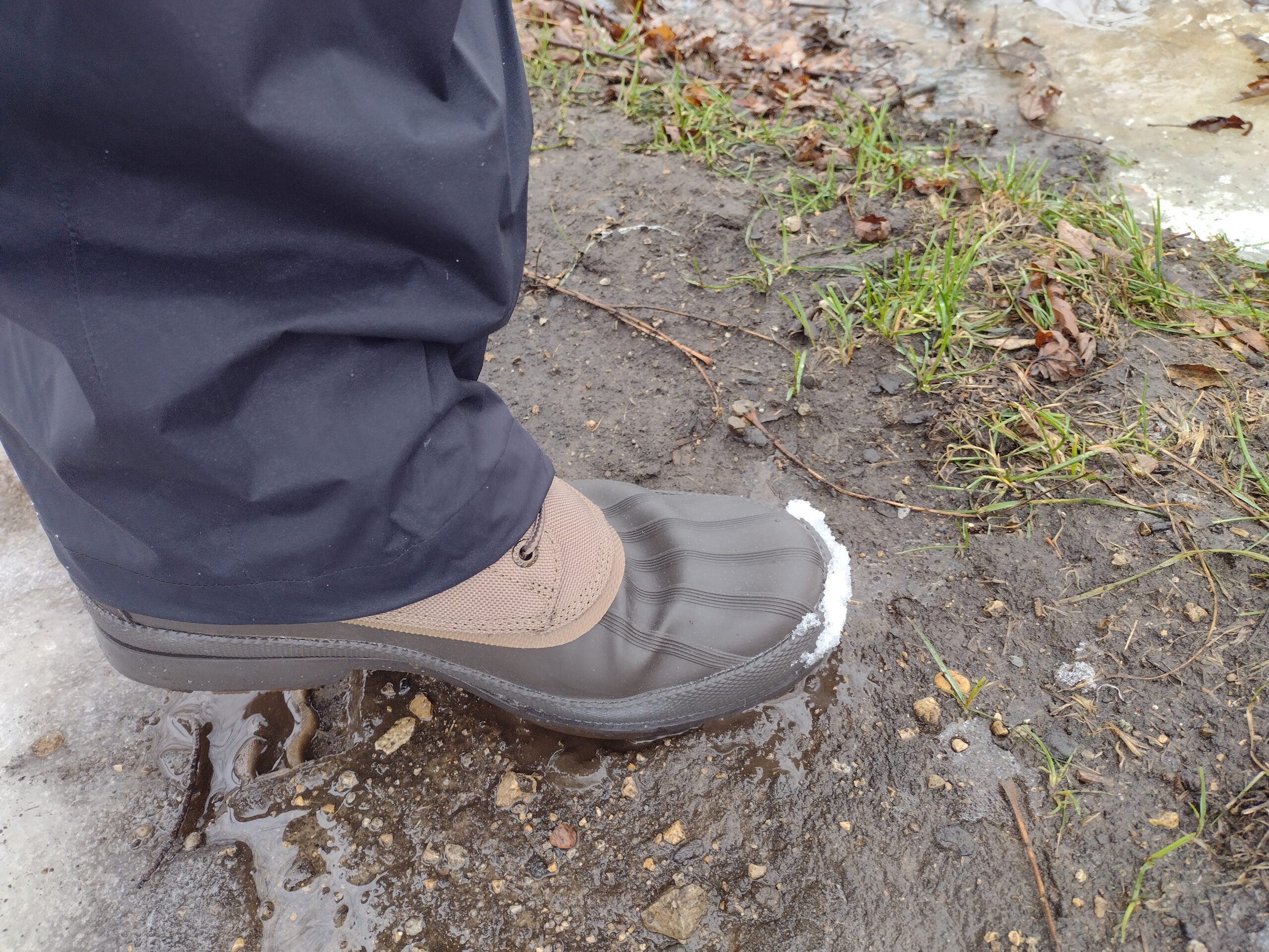 Ground level view of someone wearing the brown Sperry Cold Bay Chukka on mud and ice.
