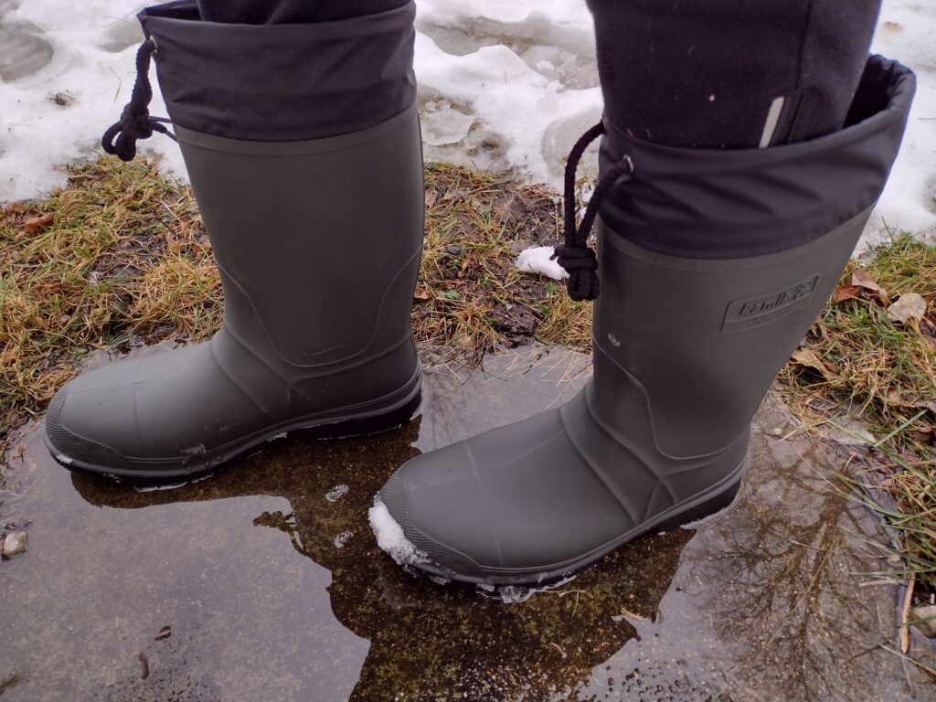 Ground level view of someone wearing the green Kamik Forester in a puddle.