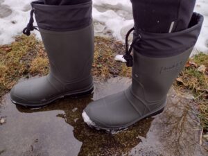 Ground level view of someone wearing the green Kamik Forester in a puddle.