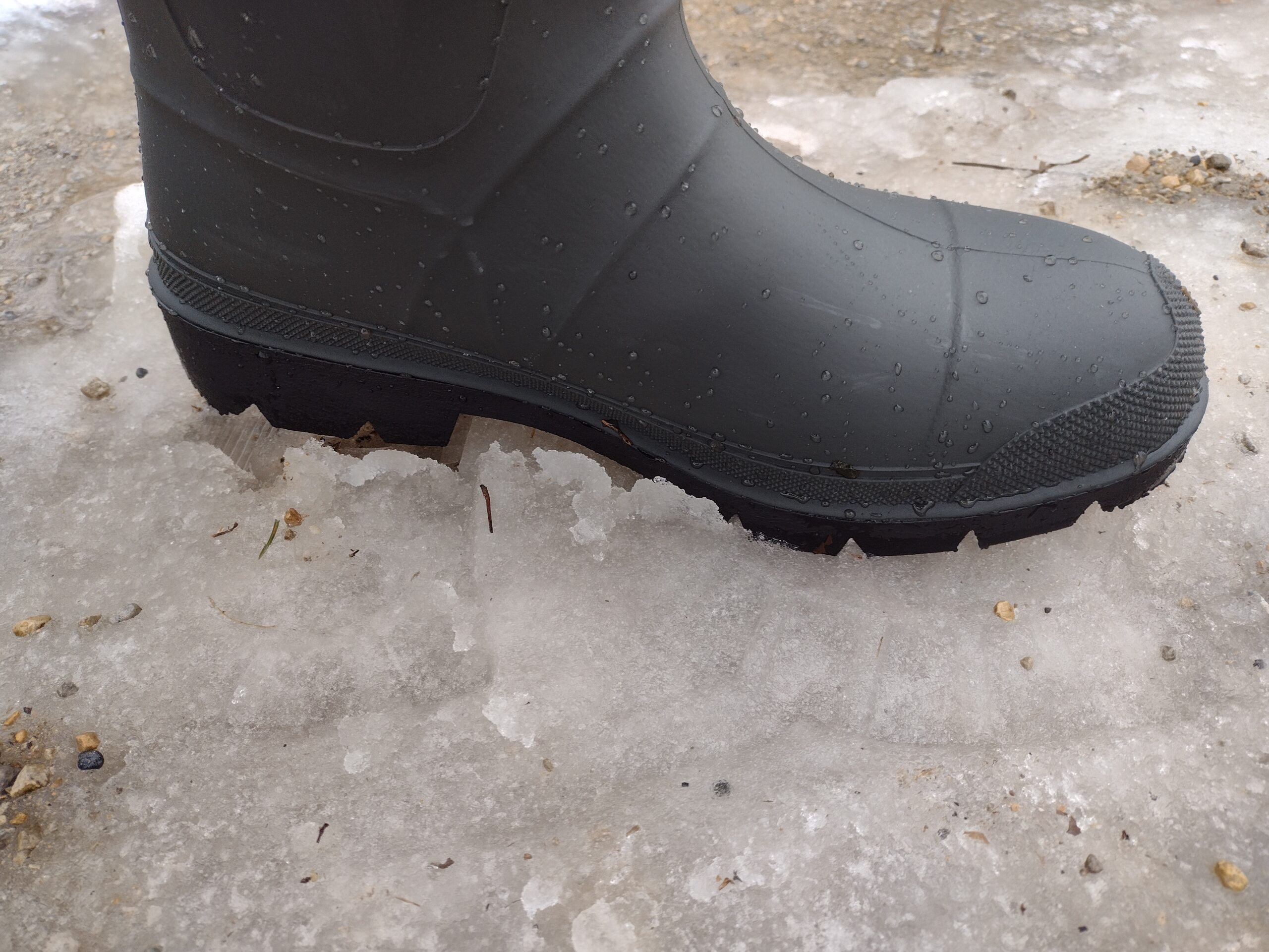 Ground level view of someone wearing the green Kamik Forester on icy slush.