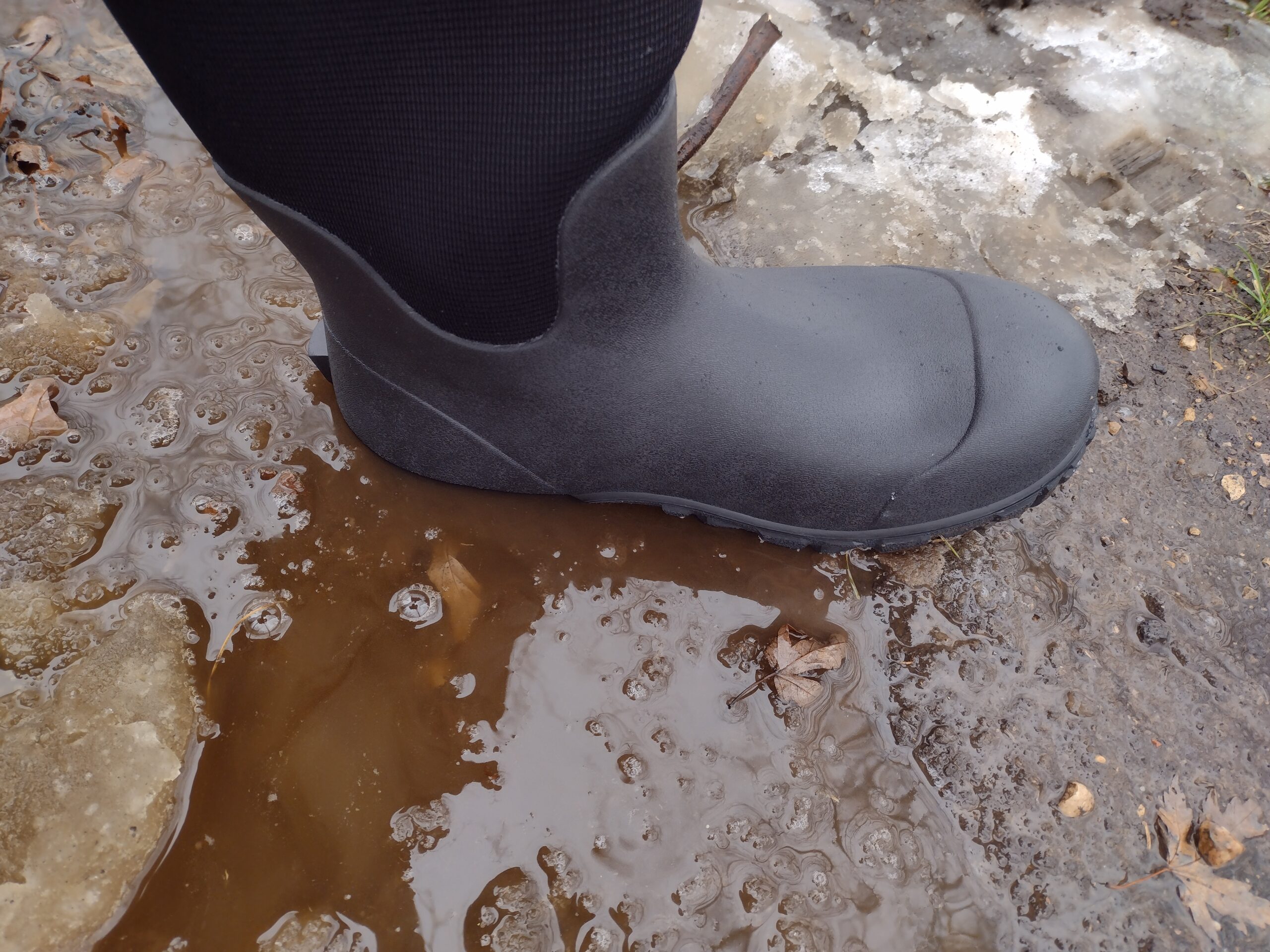 Ground level view of someone wearing the black Bogs Workman in muddy snow and water.