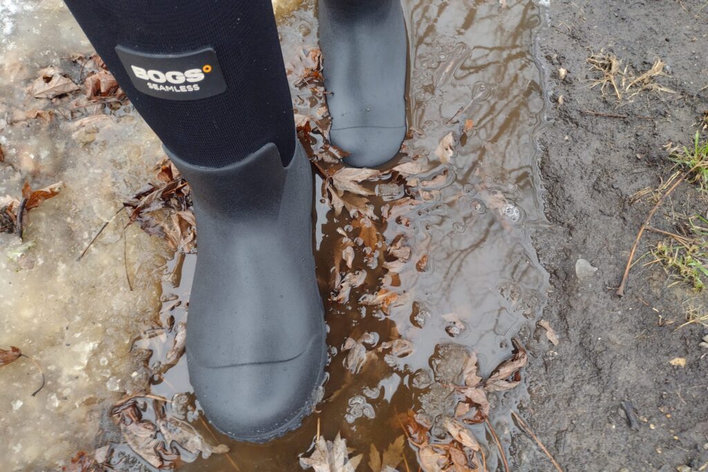 Ground level view of someone wearing the black Bogs Workman in muddy snow and water.