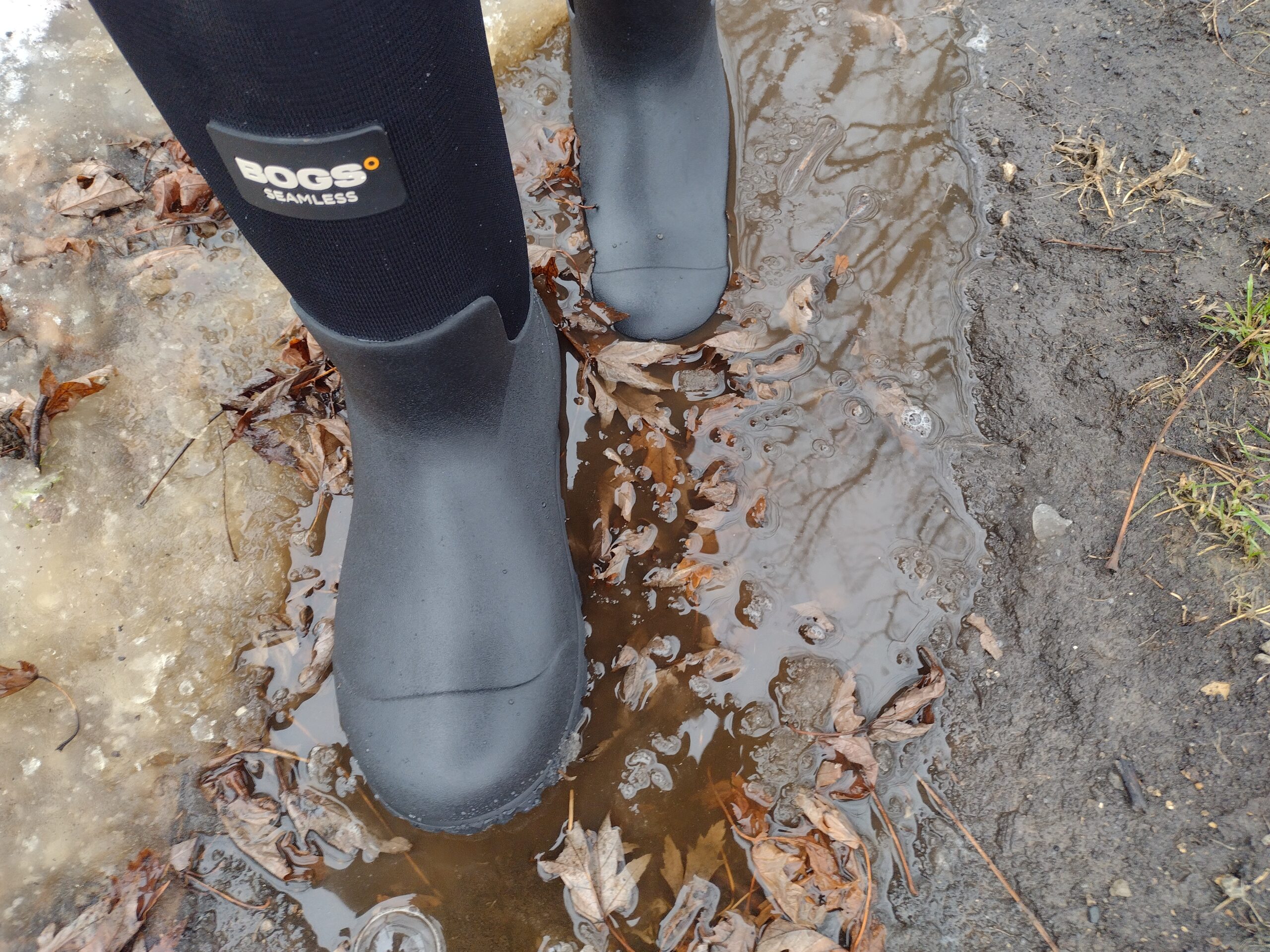 Ground level view of someone wearing the black Bogs Workman in muddy snow and water.