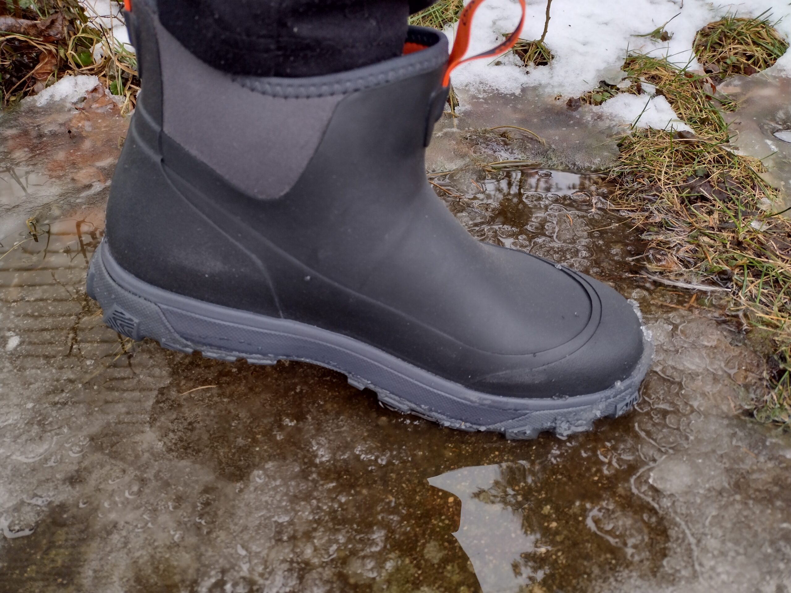 Ground level view of someone wearing the black Grundens Deviation Ankle Boot in icy water.